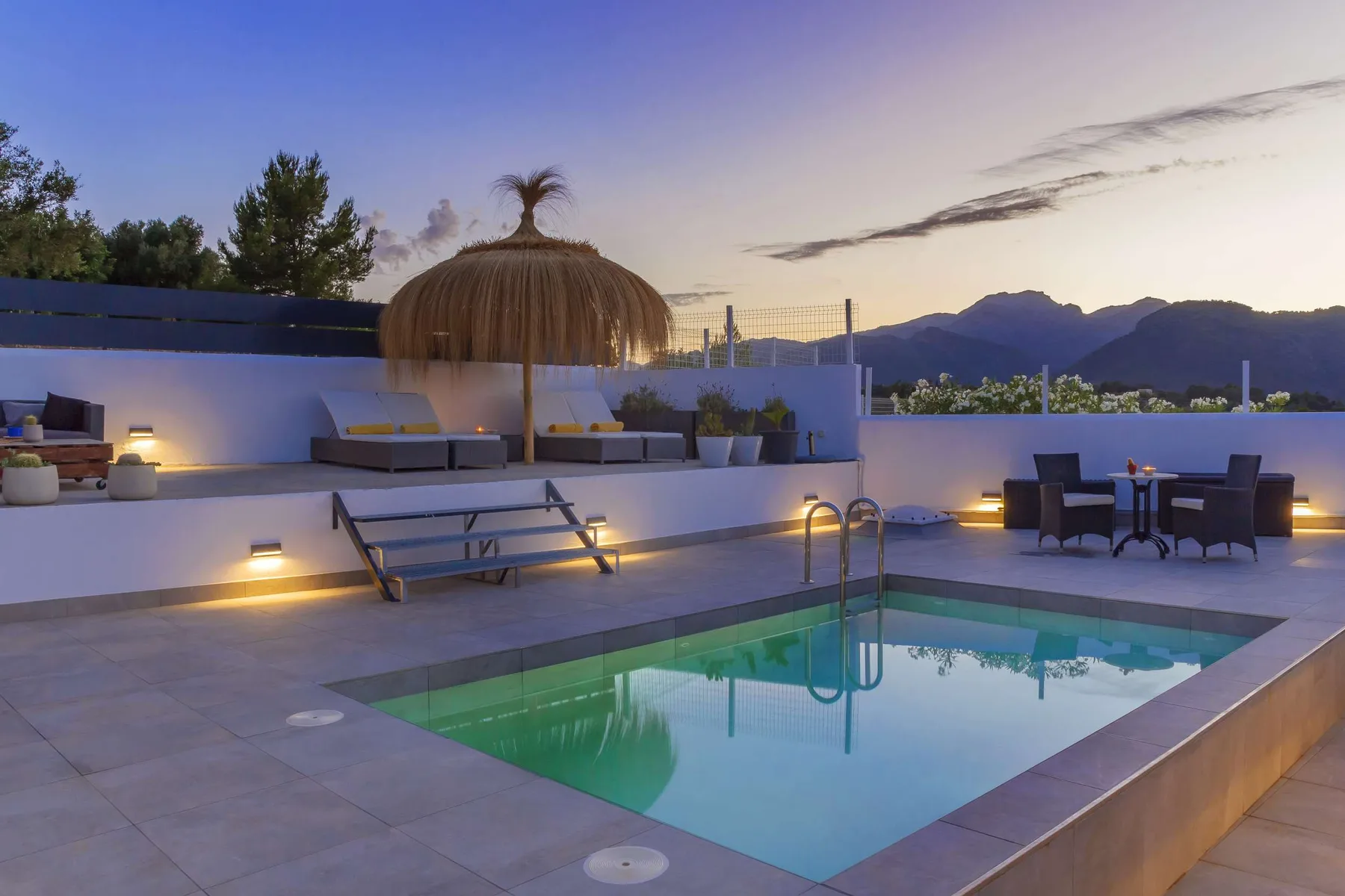 A rooftop pool terrace with loungers and outdoor seating at dusk.
