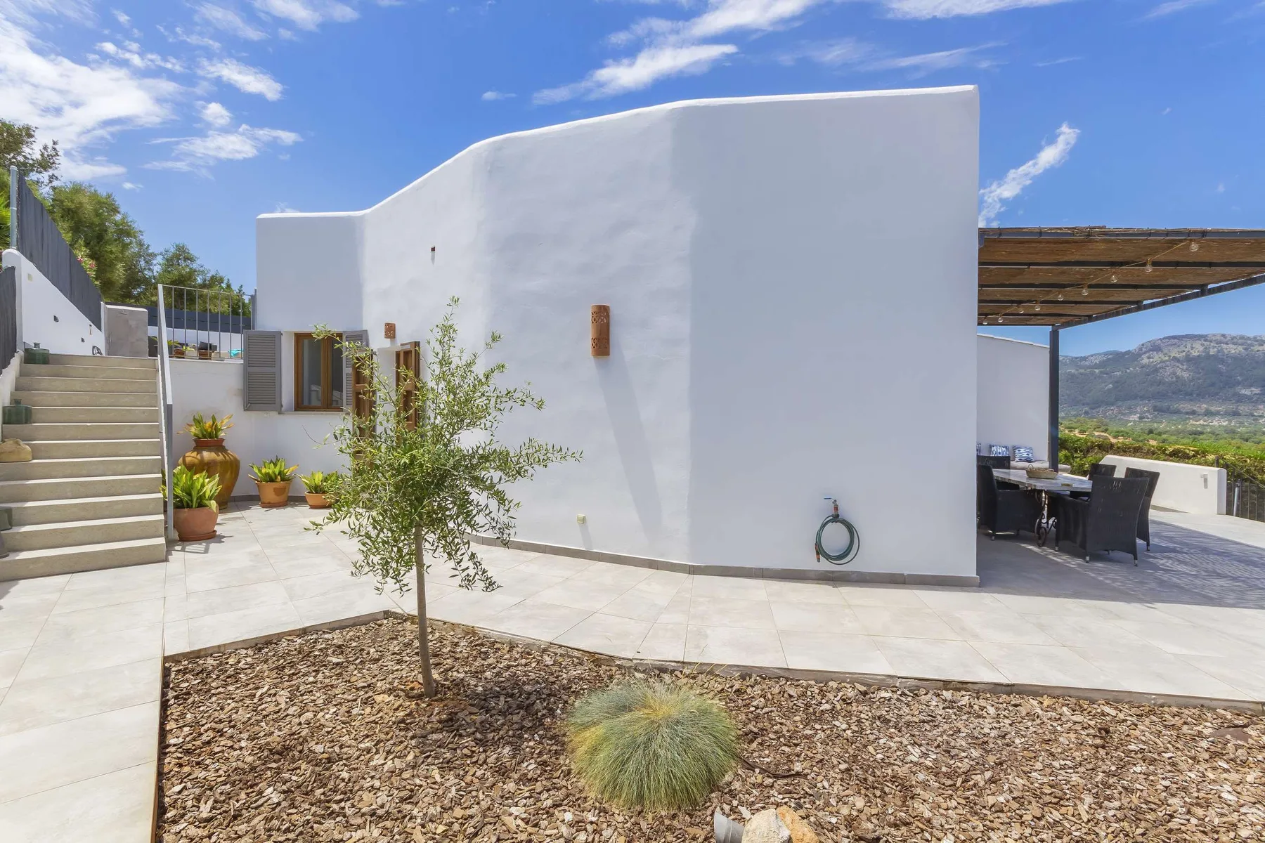 A modern white exterior opens onto a patio with outdoor seating and a mountain view.