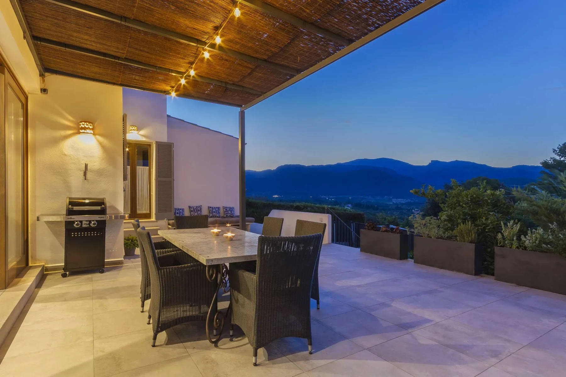 A covered outdoor dining terrace overlooks a mountain landscape at dusk.