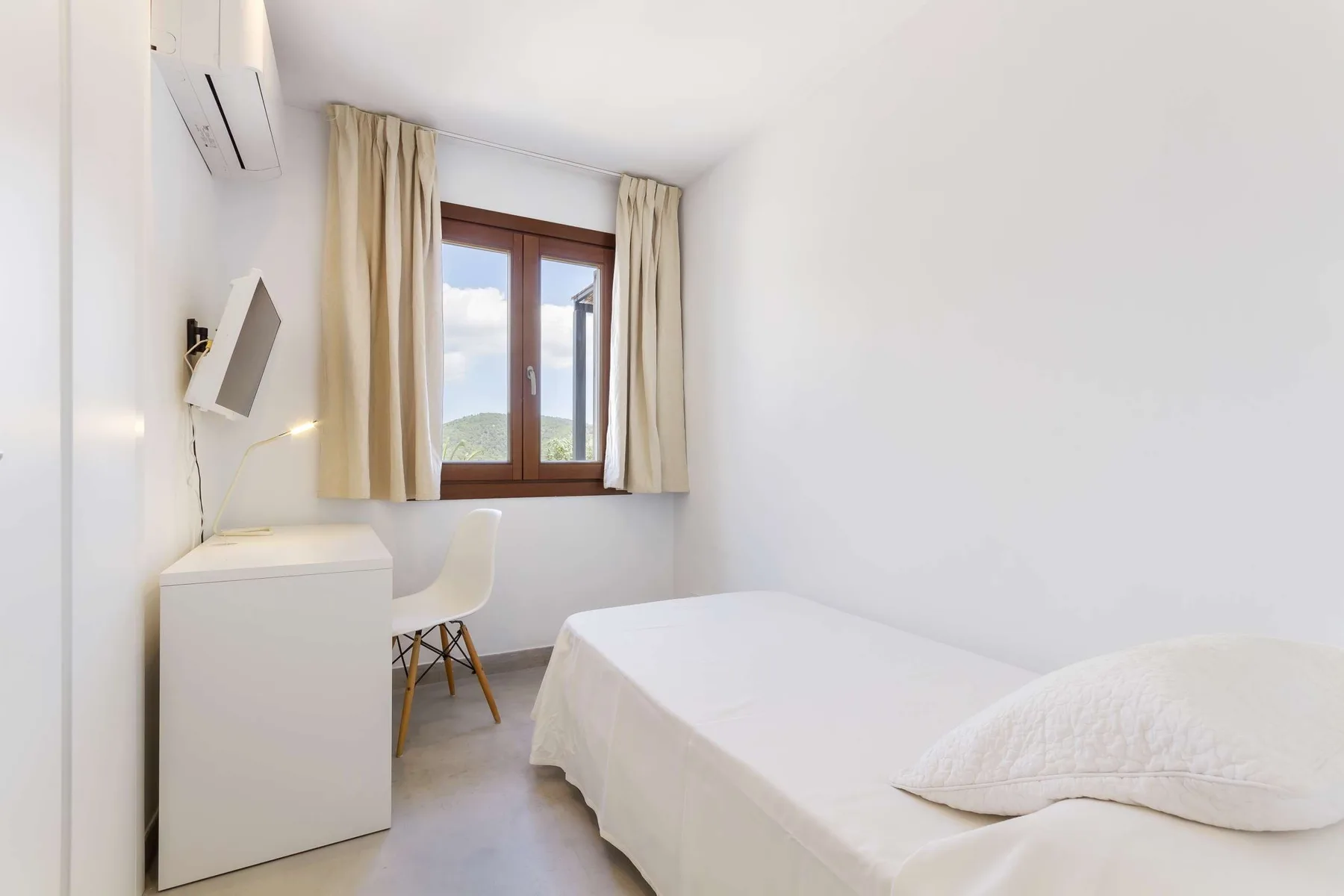 A bright bedroom with a bed, desk, and window with curtains.