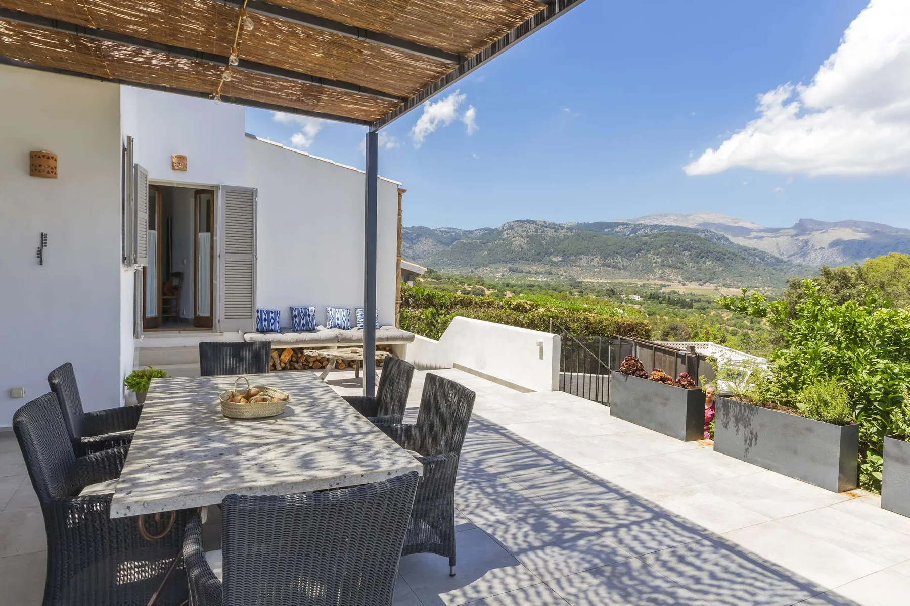 An outdoor dining area under a shaded pergola overlooks a green mountain landscape.