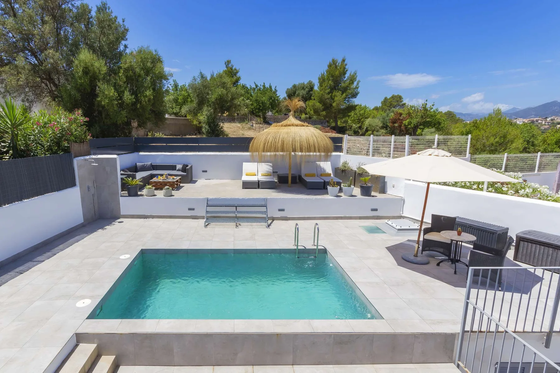 Outdoor pool area with lounge seating, umbrellas, and surrounding trees.