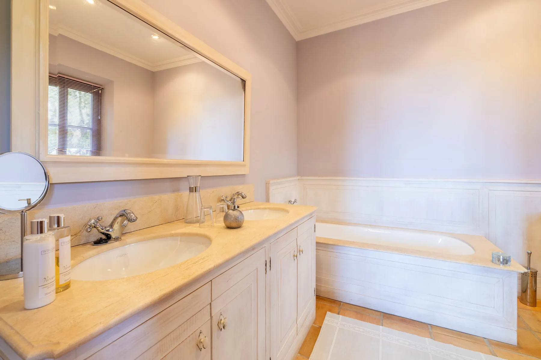 A bathroom with a double-sink vanity, large mirror, and bathtub.