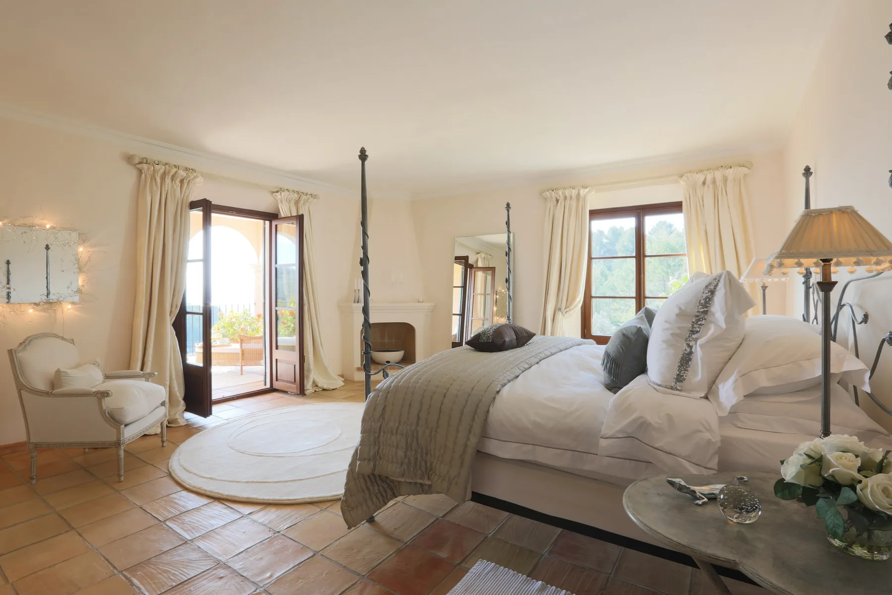 A bright bedroom with a large bed, tall windows, and a small seating area.