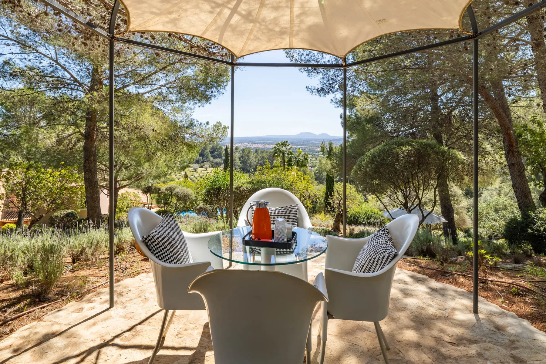 An outdoor dining area with seating and a table overlooks a green landscape.