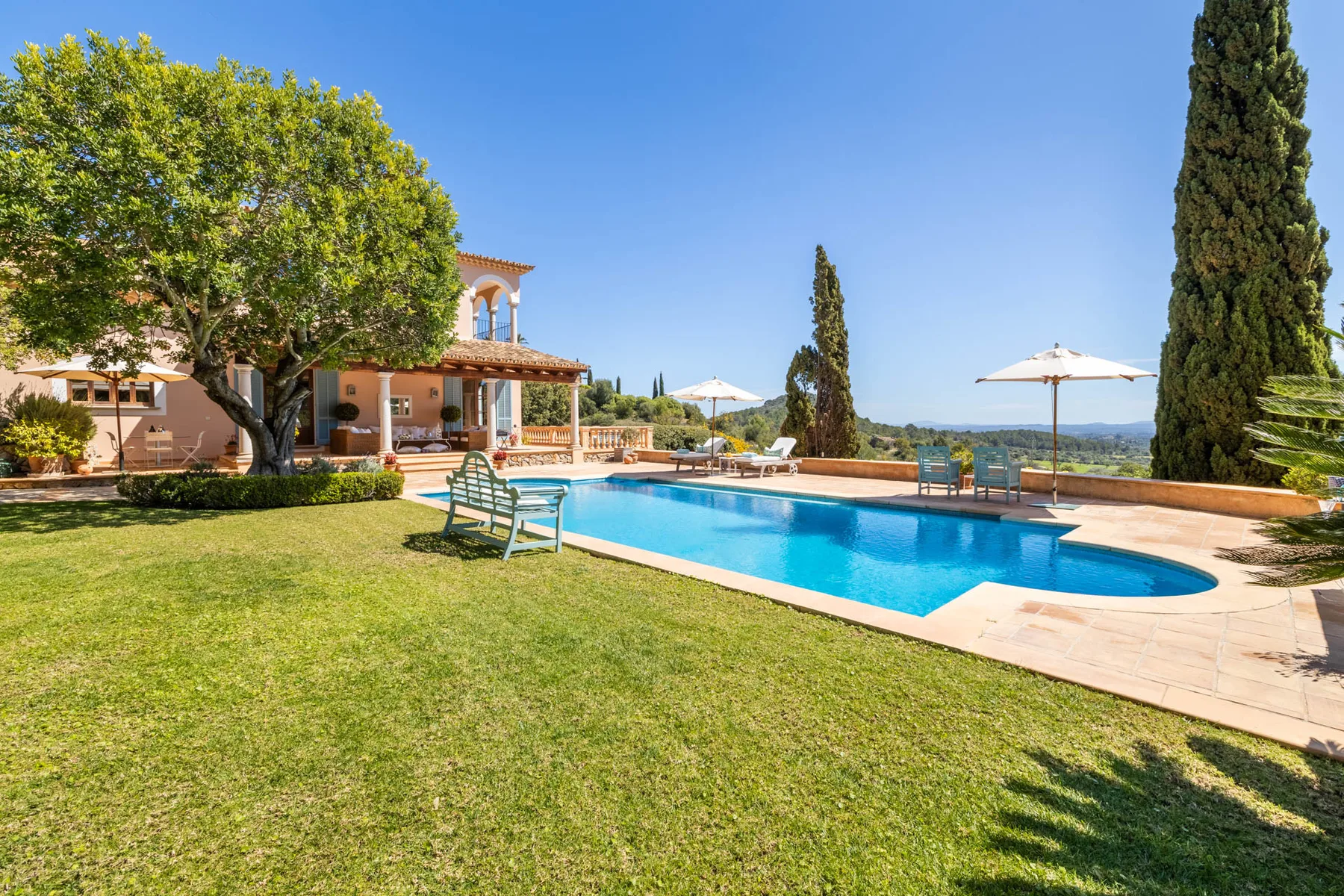 An outdoor swimming pool beside a lawn, with a house and trees nearby.