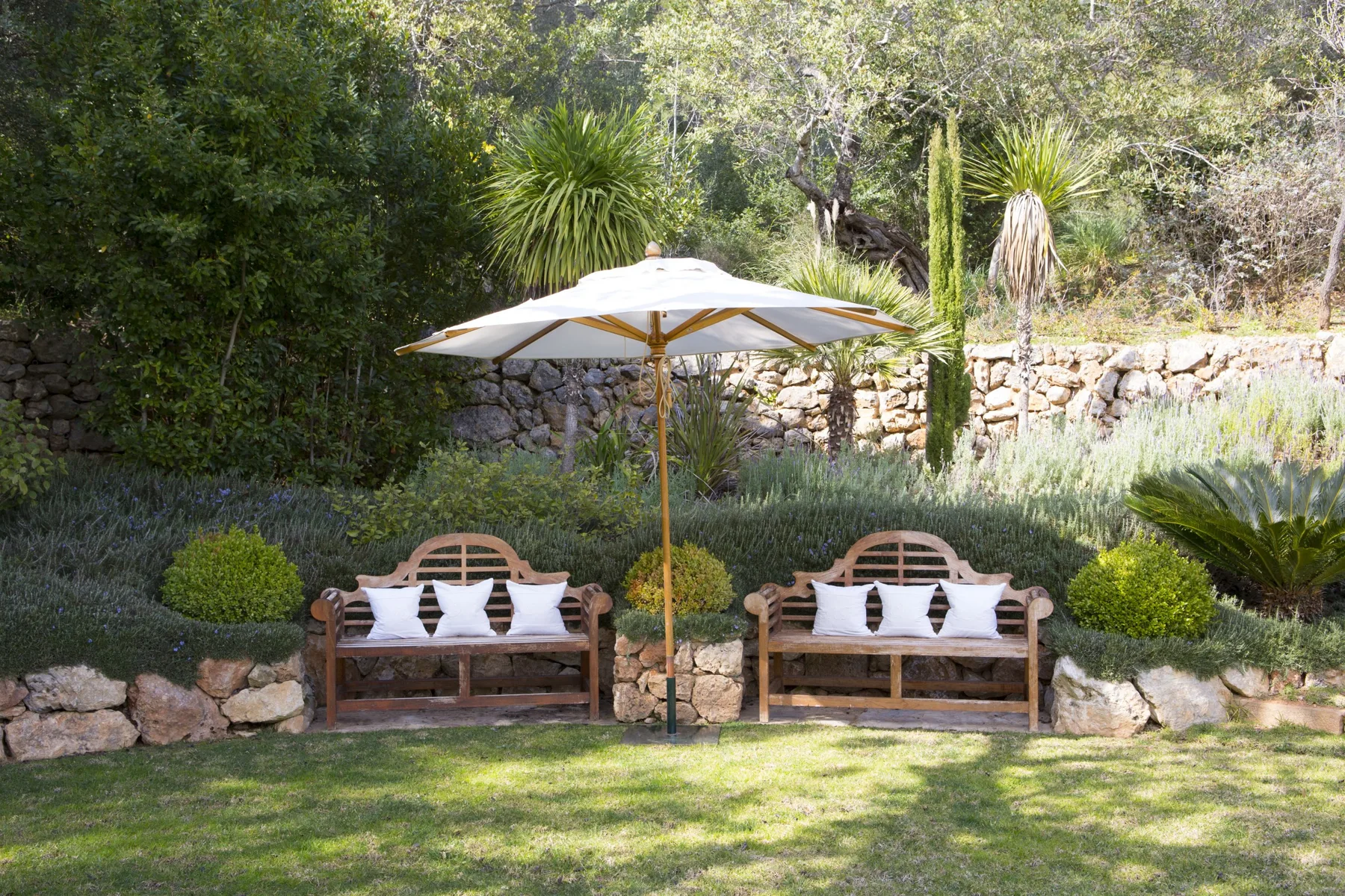 A garden seating area with two wooden benches beneath a large sun umbrella.