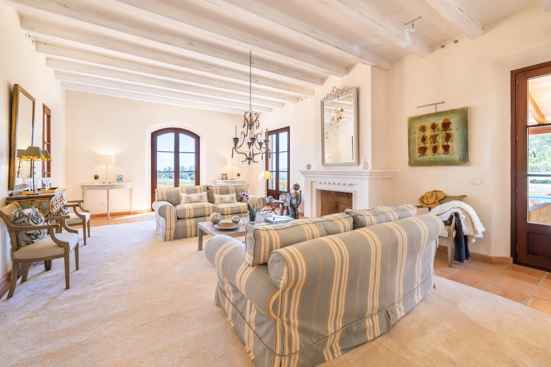 A bright living room with striped seating, a fireplace, and large arched windows.