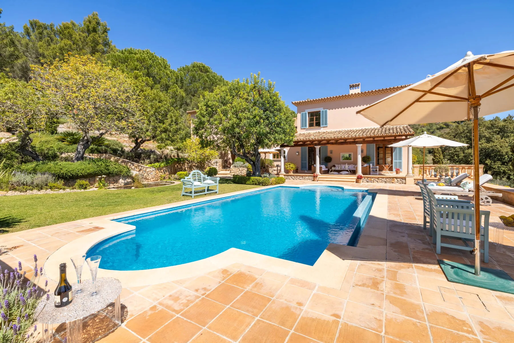 An outdoor swimming pool beside a house, with patio seating and parasols.