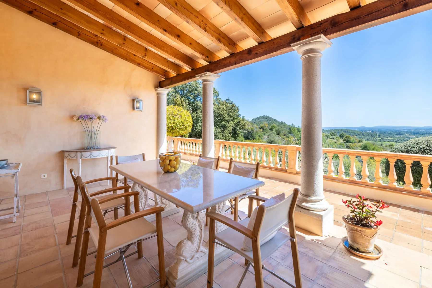 A covered terrace with a dining table overlooks a green landscape.
