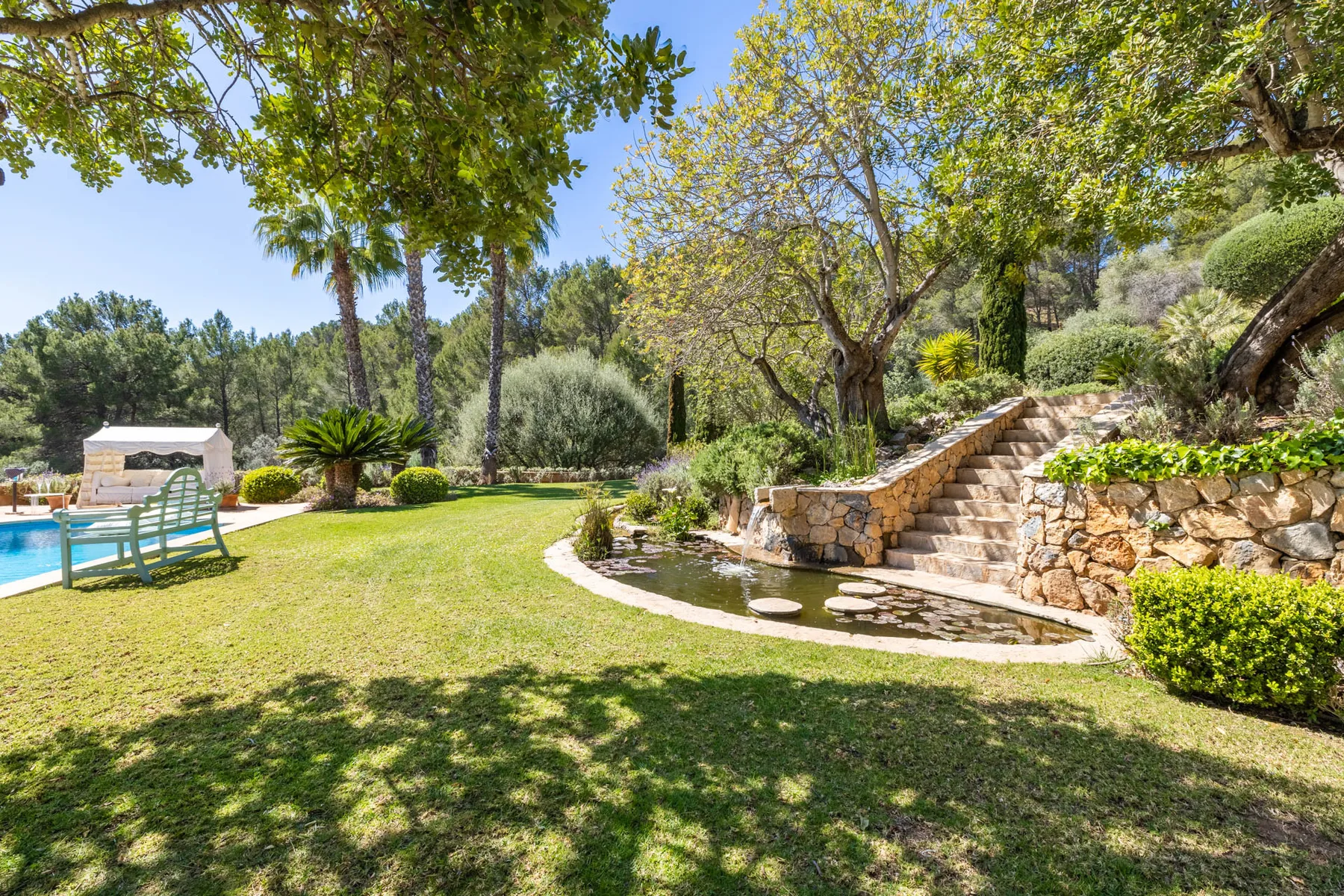 A landscaped garden with stone steps and a swimming pool beside the lawn.