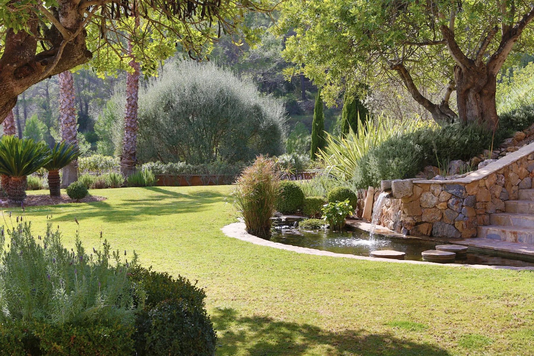 A landscaped garden with a lawn, mature trees, and a small waterfall.