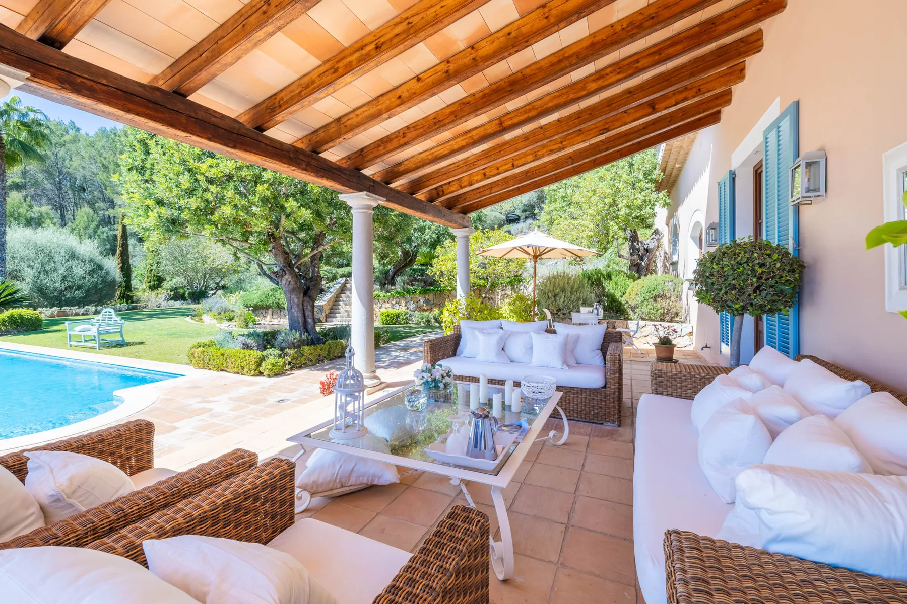 A covered patio with outdoor seating overlooks a swimming pool and garden.