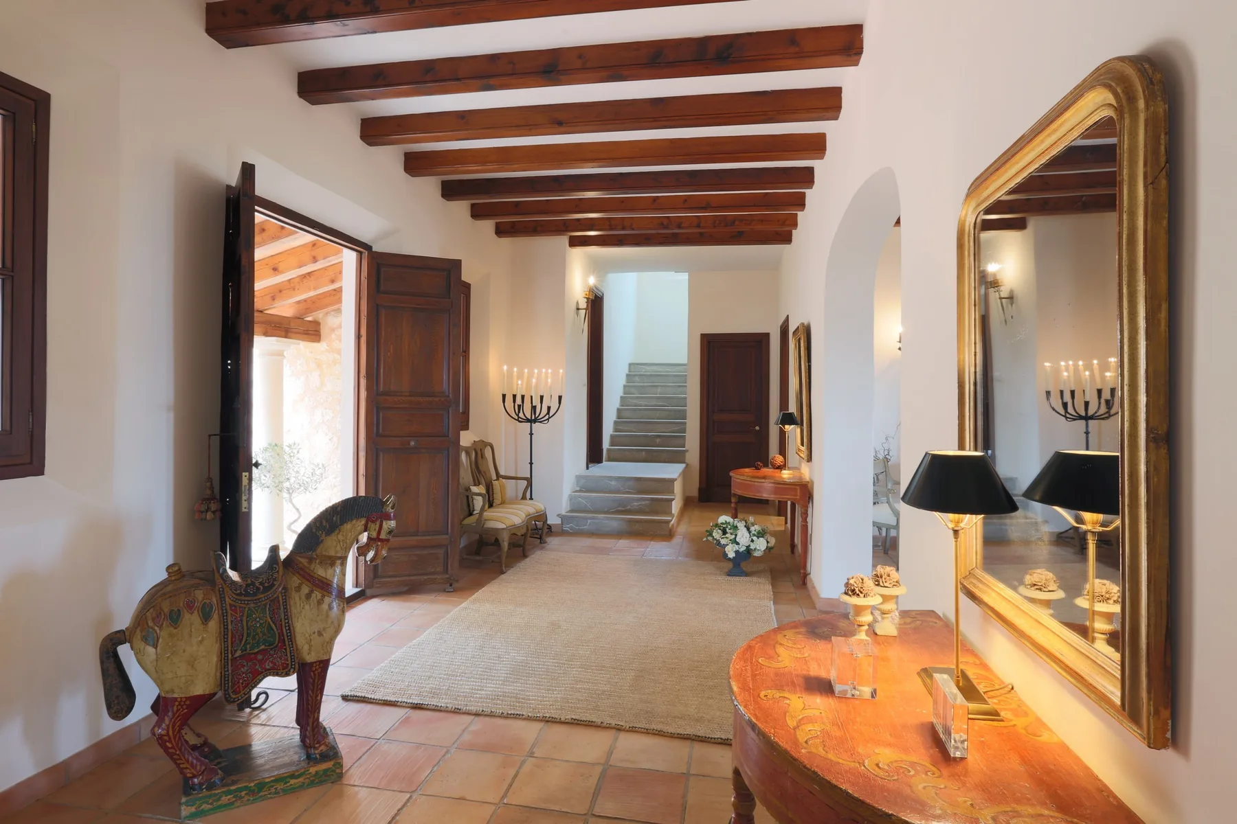 A long interior hallway with exposed wooden ceiling beams and a staircase at the far end.