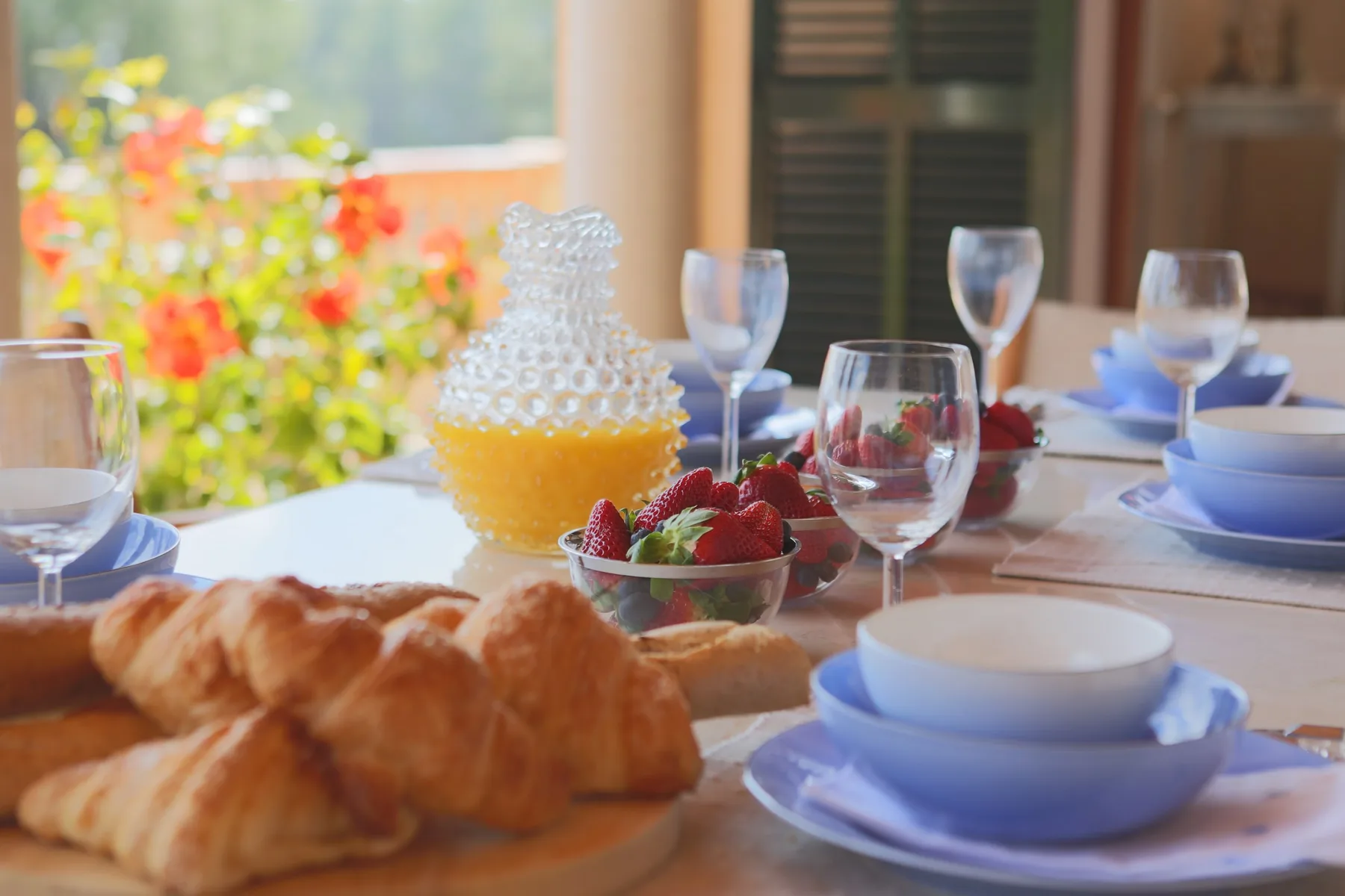 A breakfast table is set with pastries, fruit, juice, and dishes.