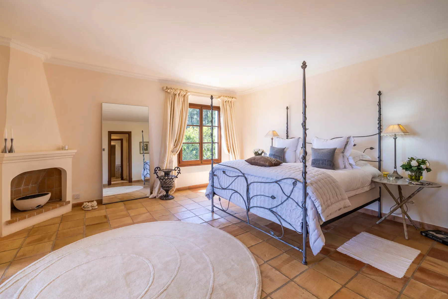 A bright bedroom with two beds, a fireplace, and a large window.