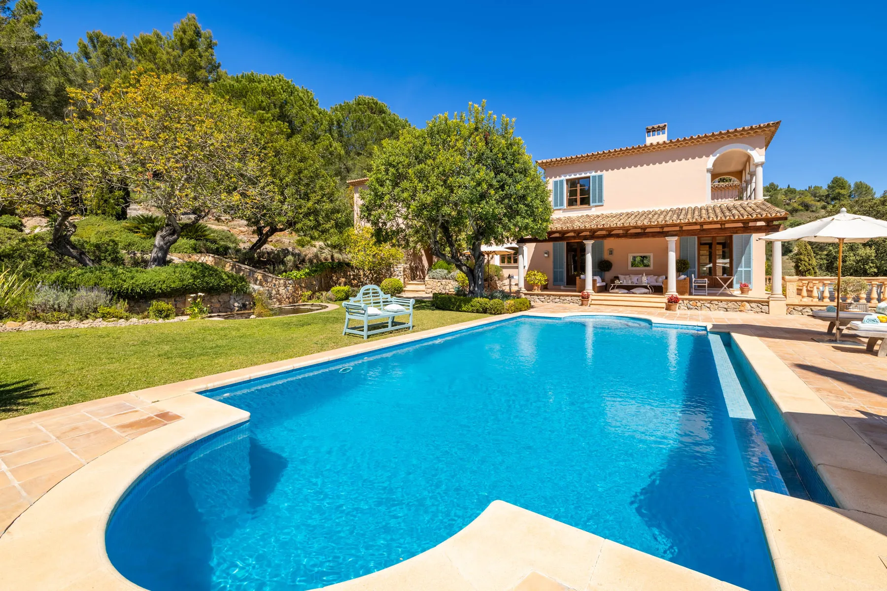 An outdoor swimming pool sits beside a landscaped garden and a house.