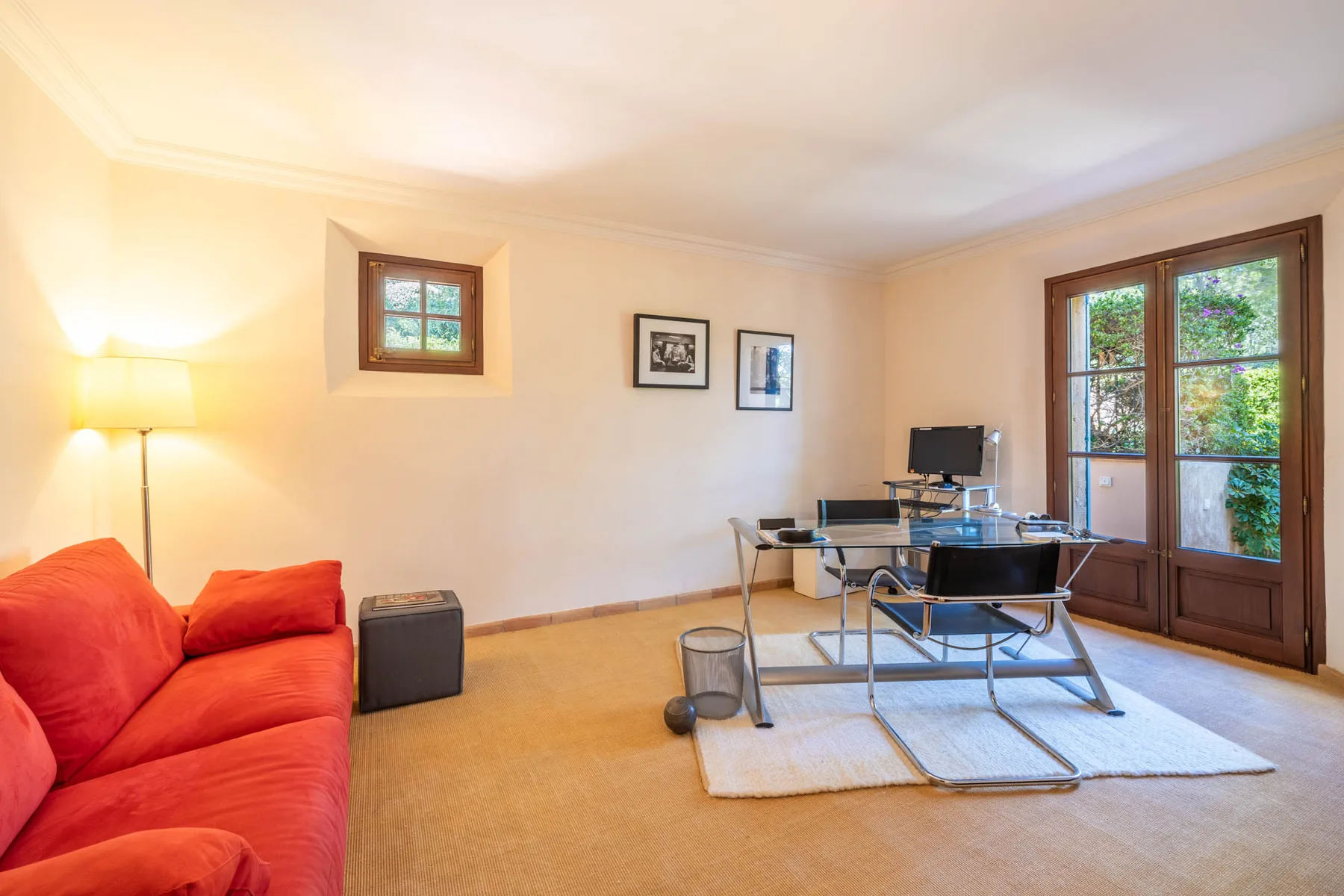 A living room with red seating and a desk beside tall windows.