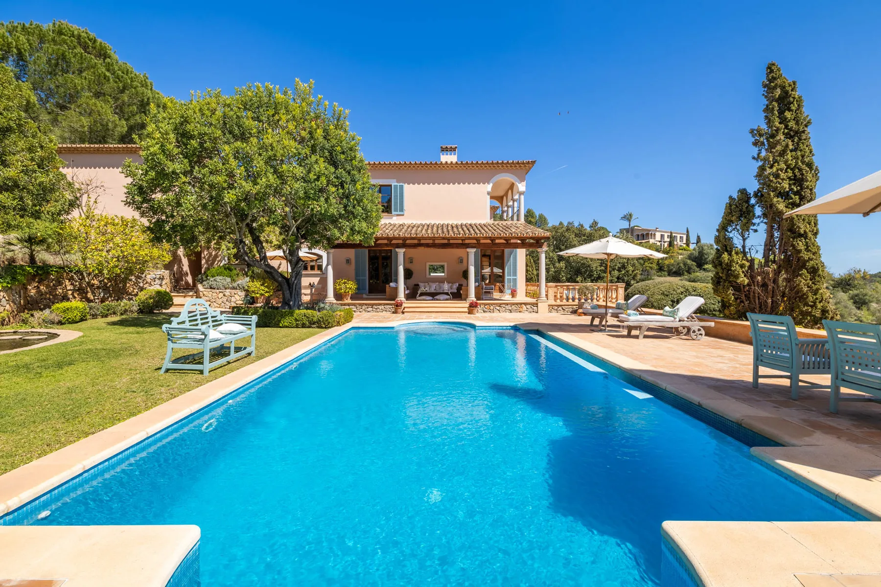 Outdoor swimming pool beside a house, with lounge seating on the patio.