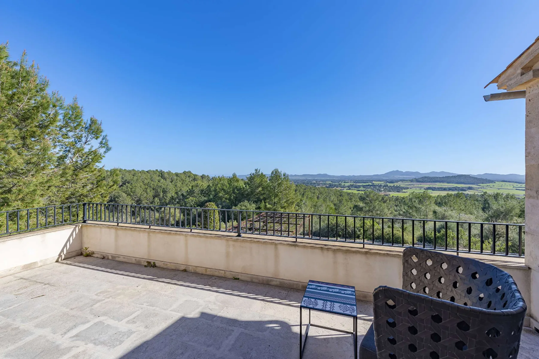 A sunlit terrace overlooks green hills, with outdoor seating beside the railing.