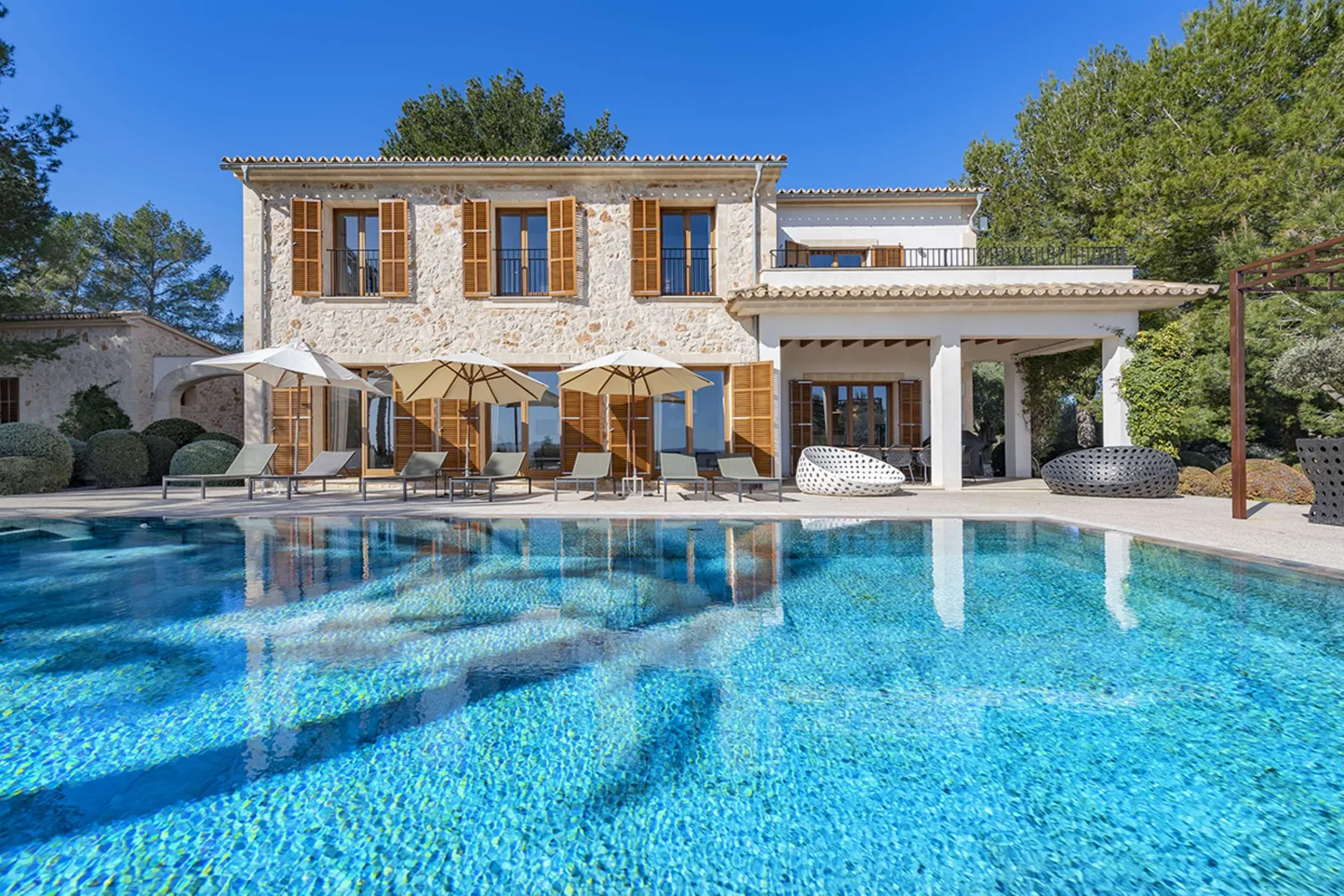 A swimming pool in front of a two-story house with a shaded patio.