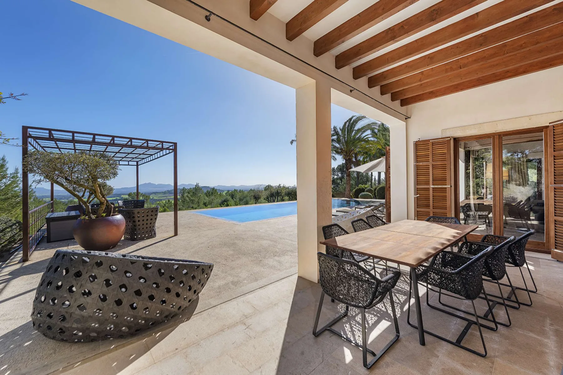 A covered patio with outdoor seating overlooks a swimming pool and distant landscape.