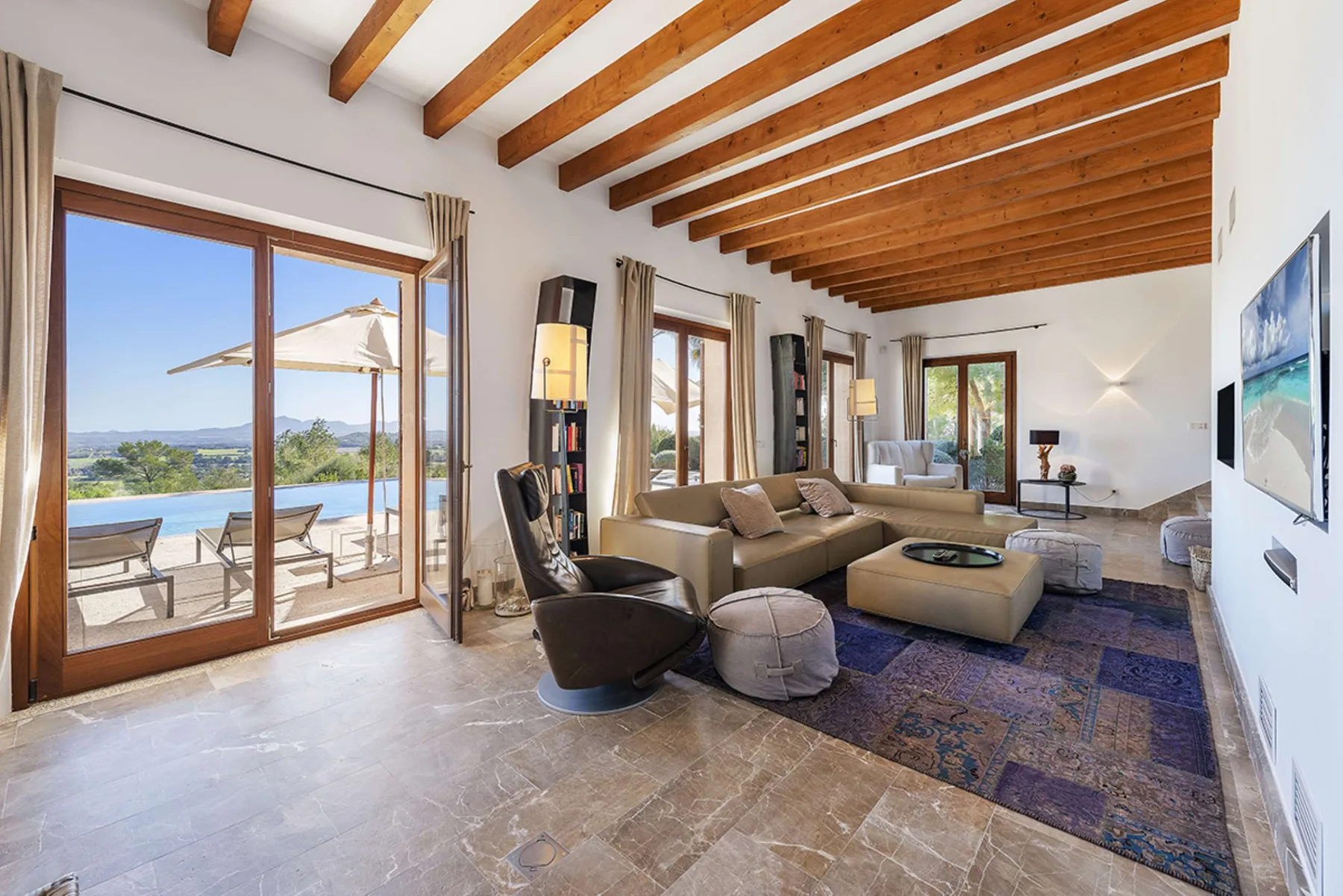 A bright living room opens onto a terrace through large glass doors.