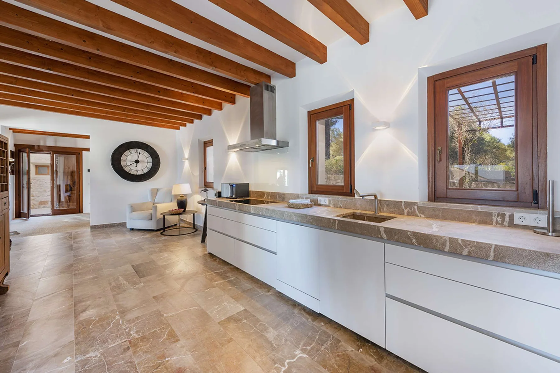 A bright kitchen with a long counter and wooden ceiling beams.