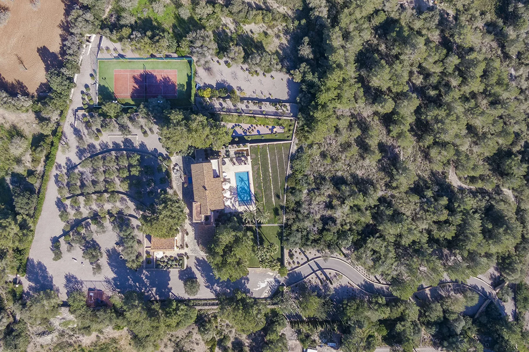 An aerial view of a wooded property with a building, swimming pool, and tennis court.