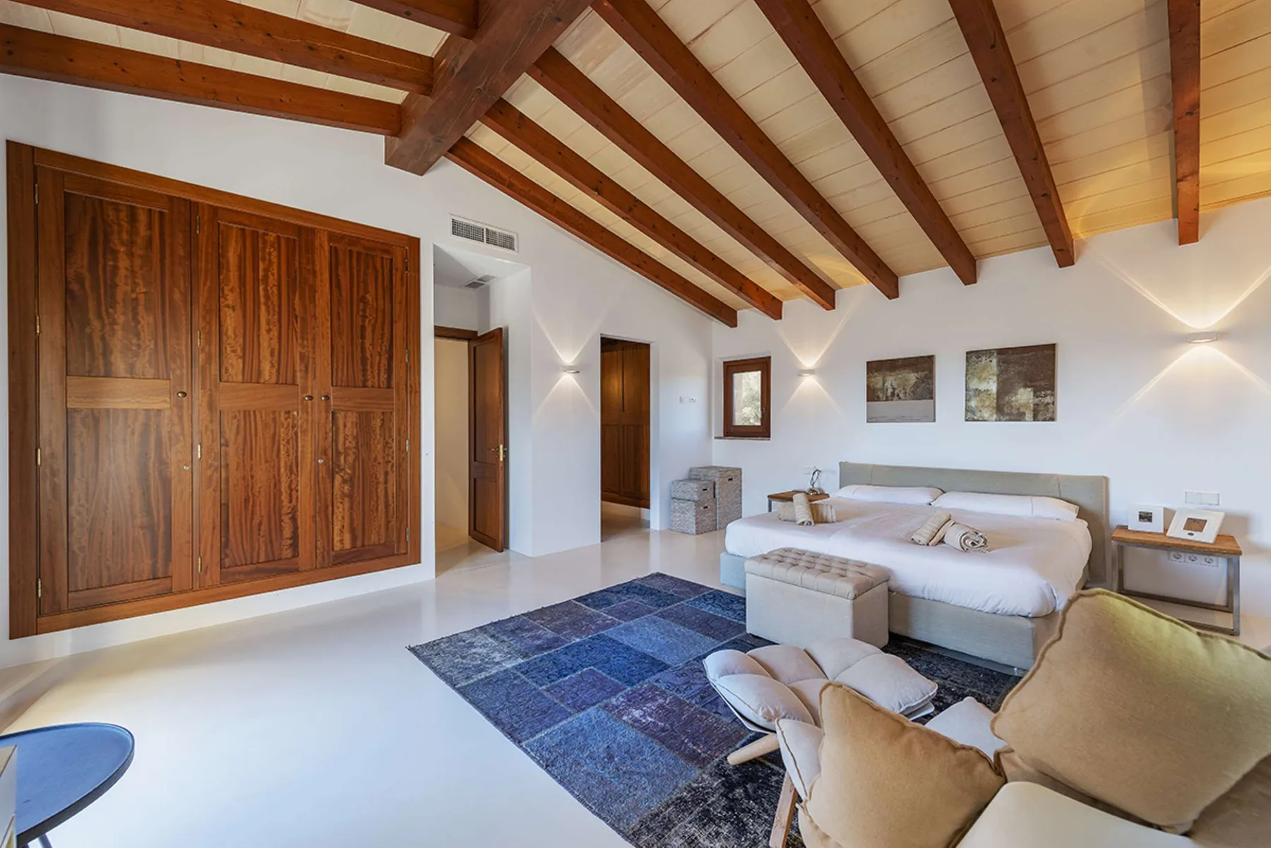 A bedroom with a bed, seating area, and exposed wooden ceiling beams.