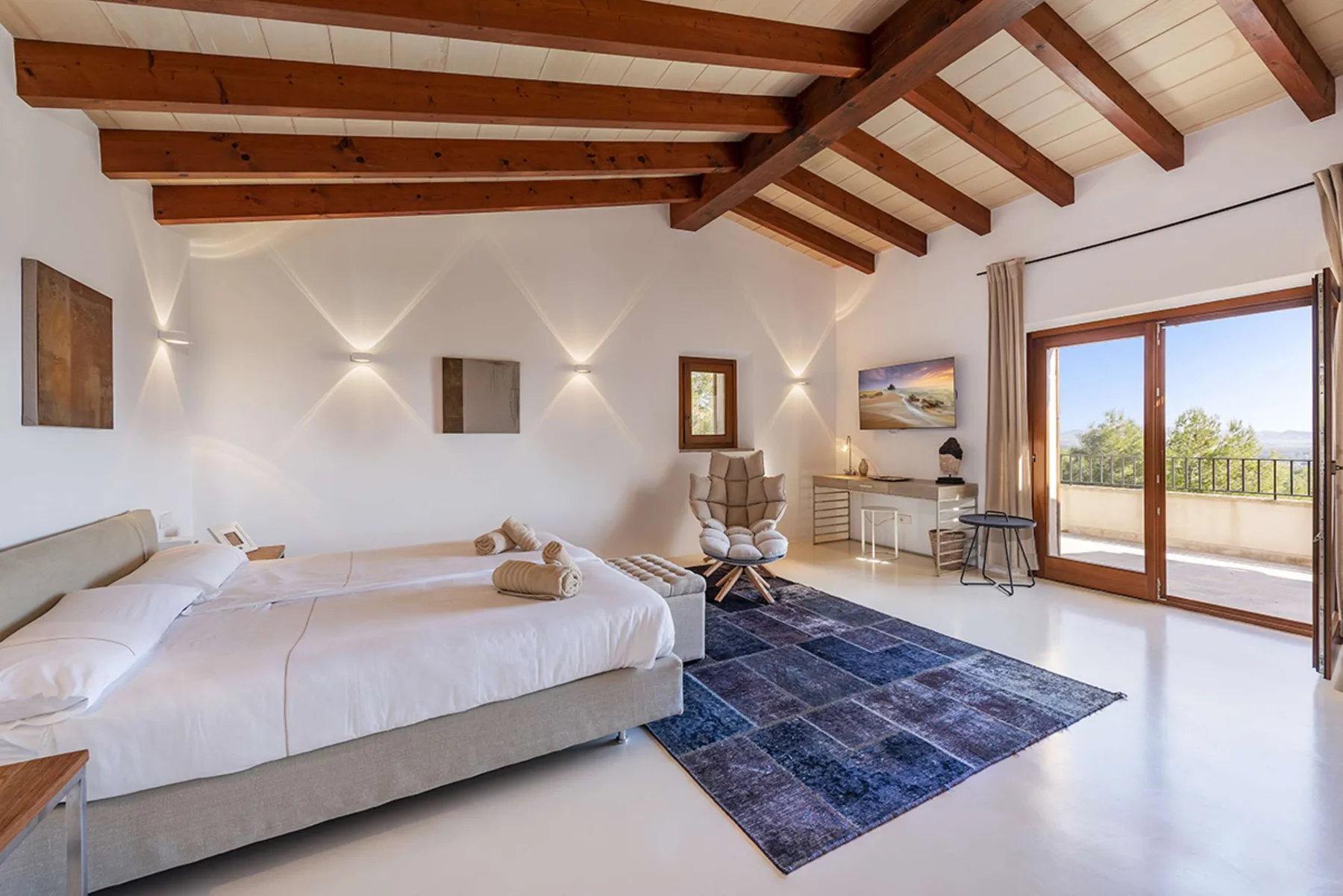 A bright bedroom with a bed, a desk, and a glass door opening onto a balcony.