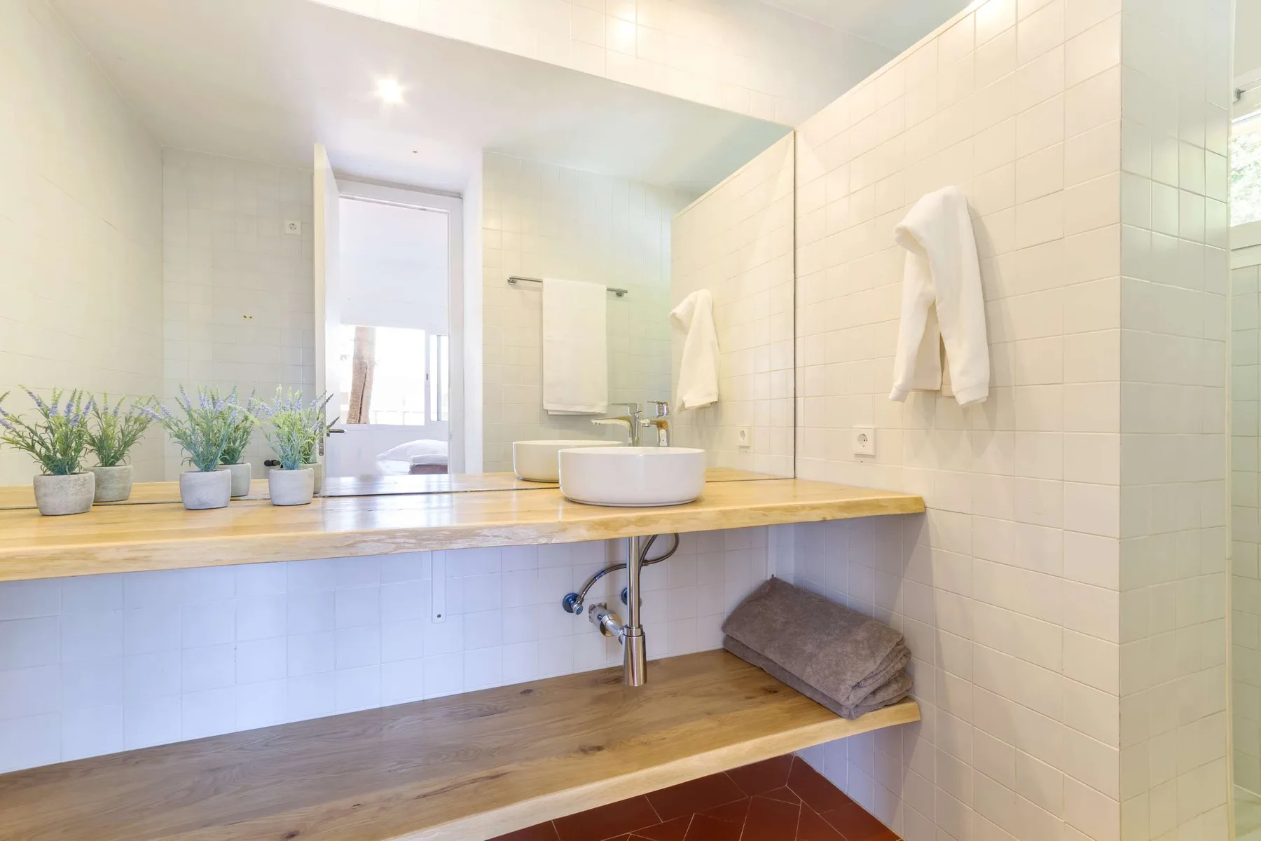 A bright tiled bathroom with a long vanity, sink, and towels.
