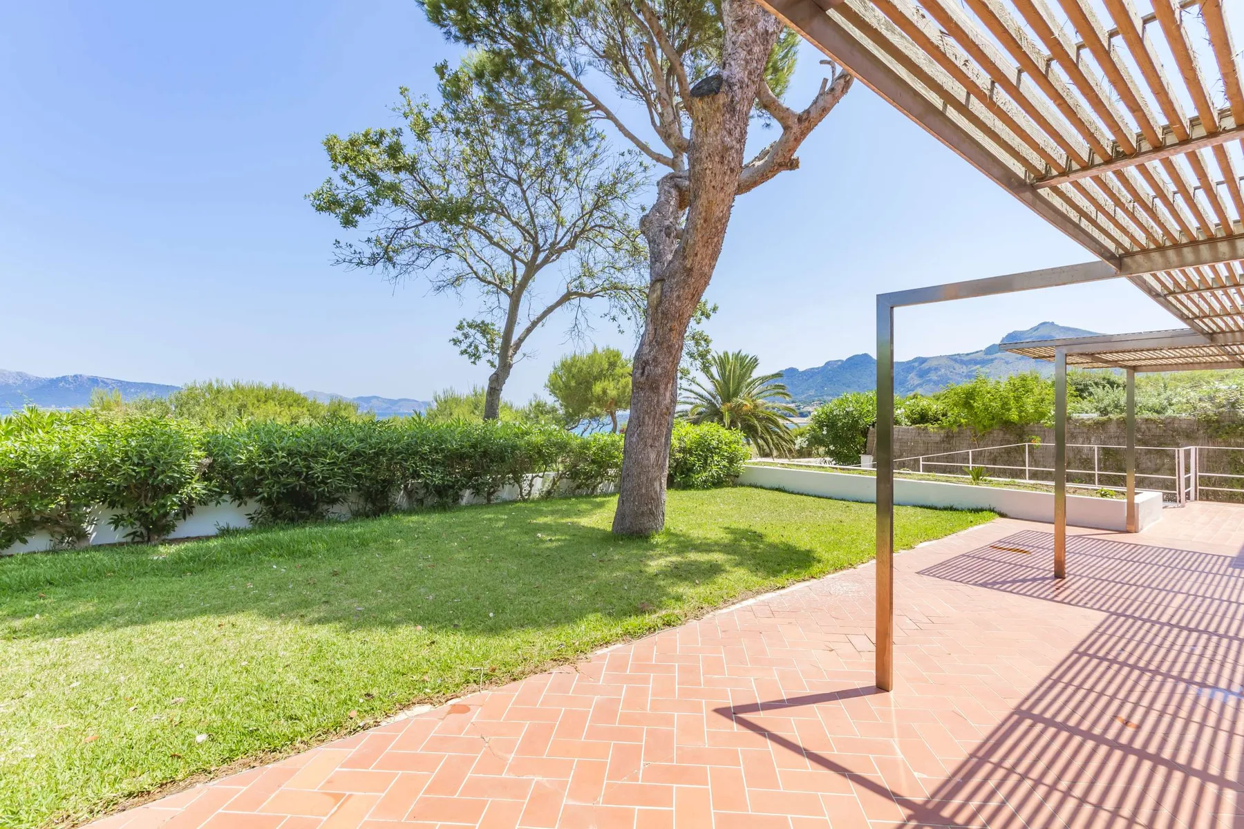 A sunny garden patio with a brick walkway, lawn, and mountain views.