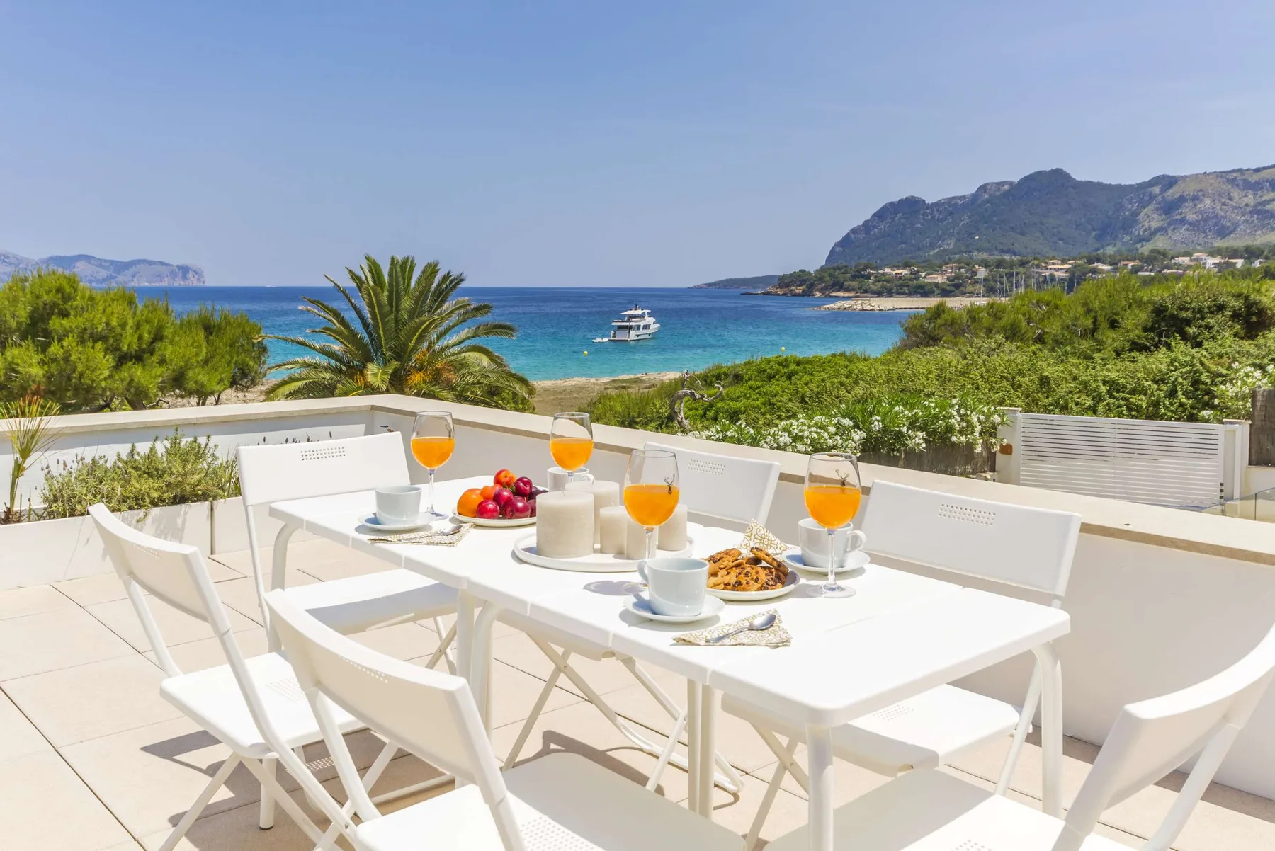 A sunny outdoor dining area overlooks the sea and a green coastline.