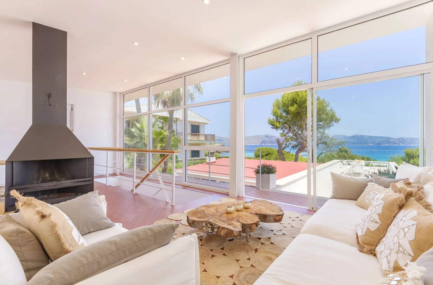 A bright living room with seating, a fireplace, and large windows overlooking the sea.