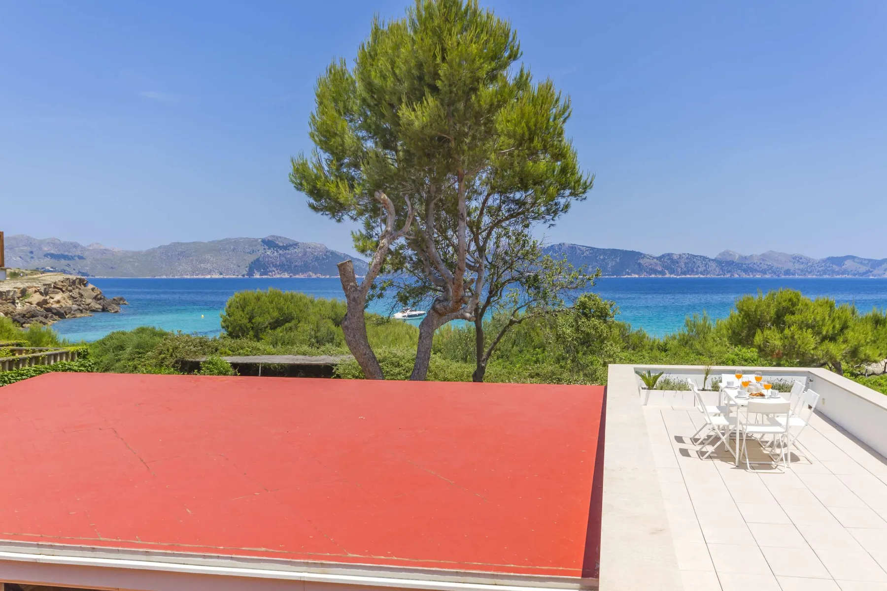 A seaside terrace has a red surface, outdoor seating, and a view of the water.