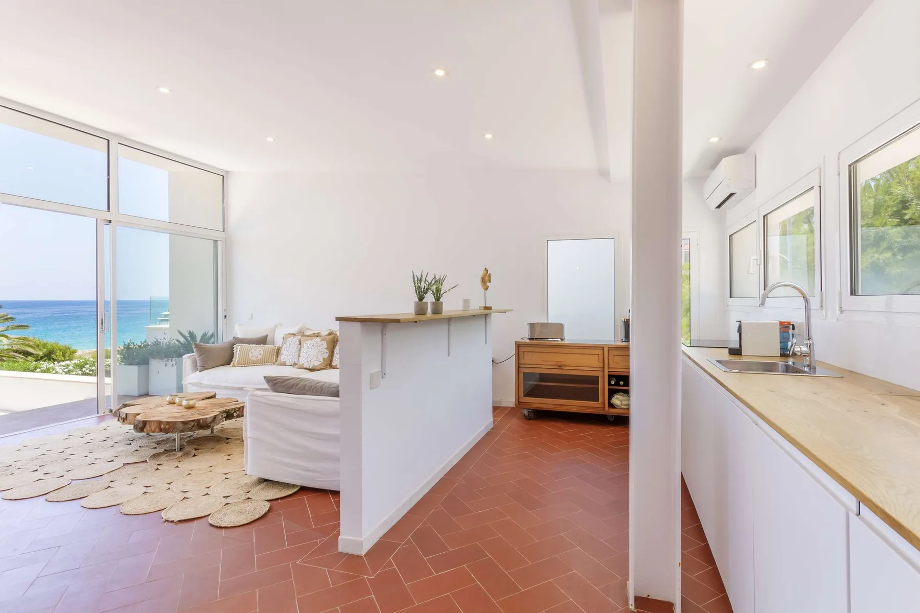 A bright open-plan living and kitchen area with large windows overlooking the sea.