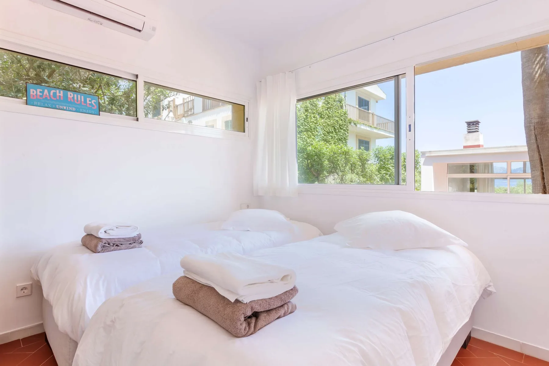 A bright bedroom with white bedding and large windows.