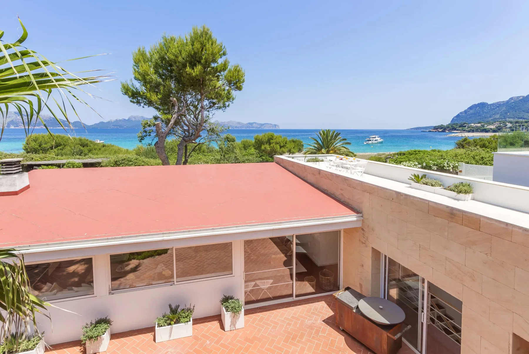 A rooftop terrace overlooks the sea, with a tree and distant hills.
