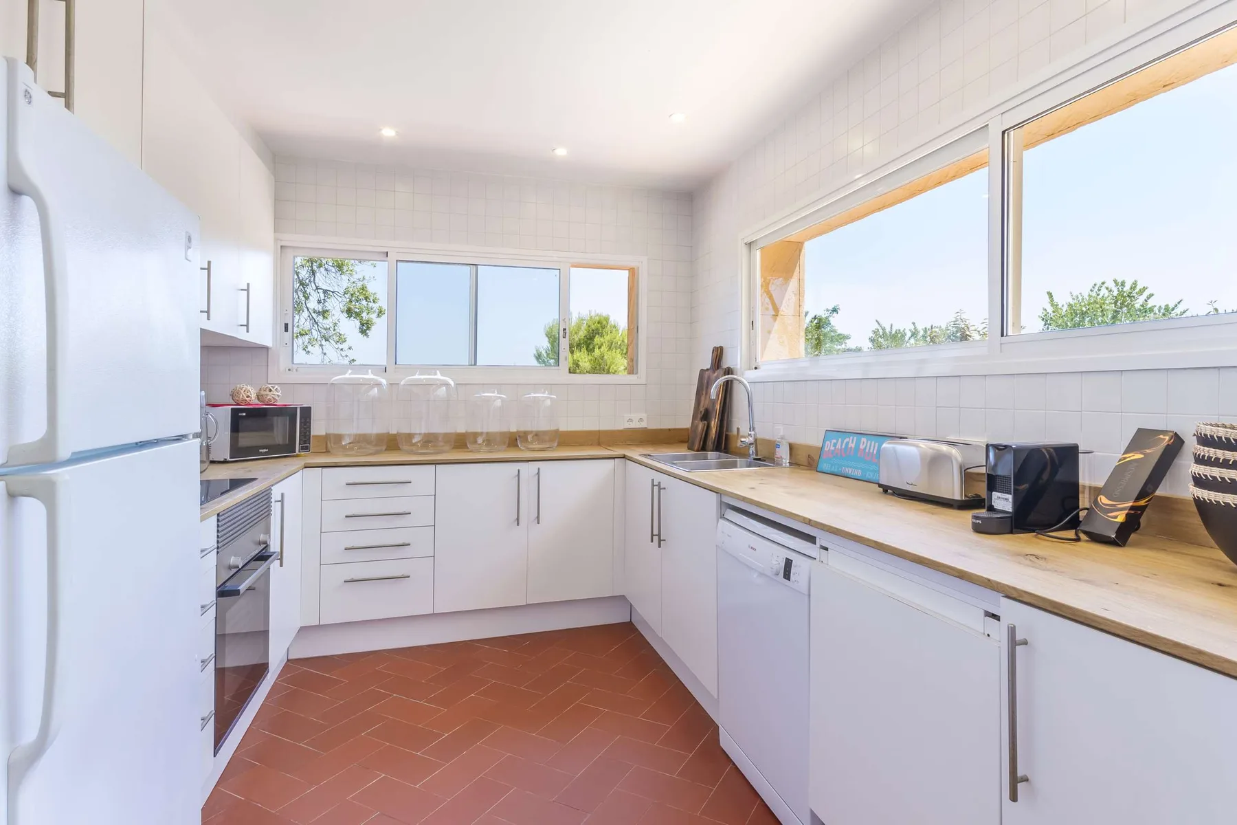 A bright kitchen with white cabinets, countertops, and large windows.