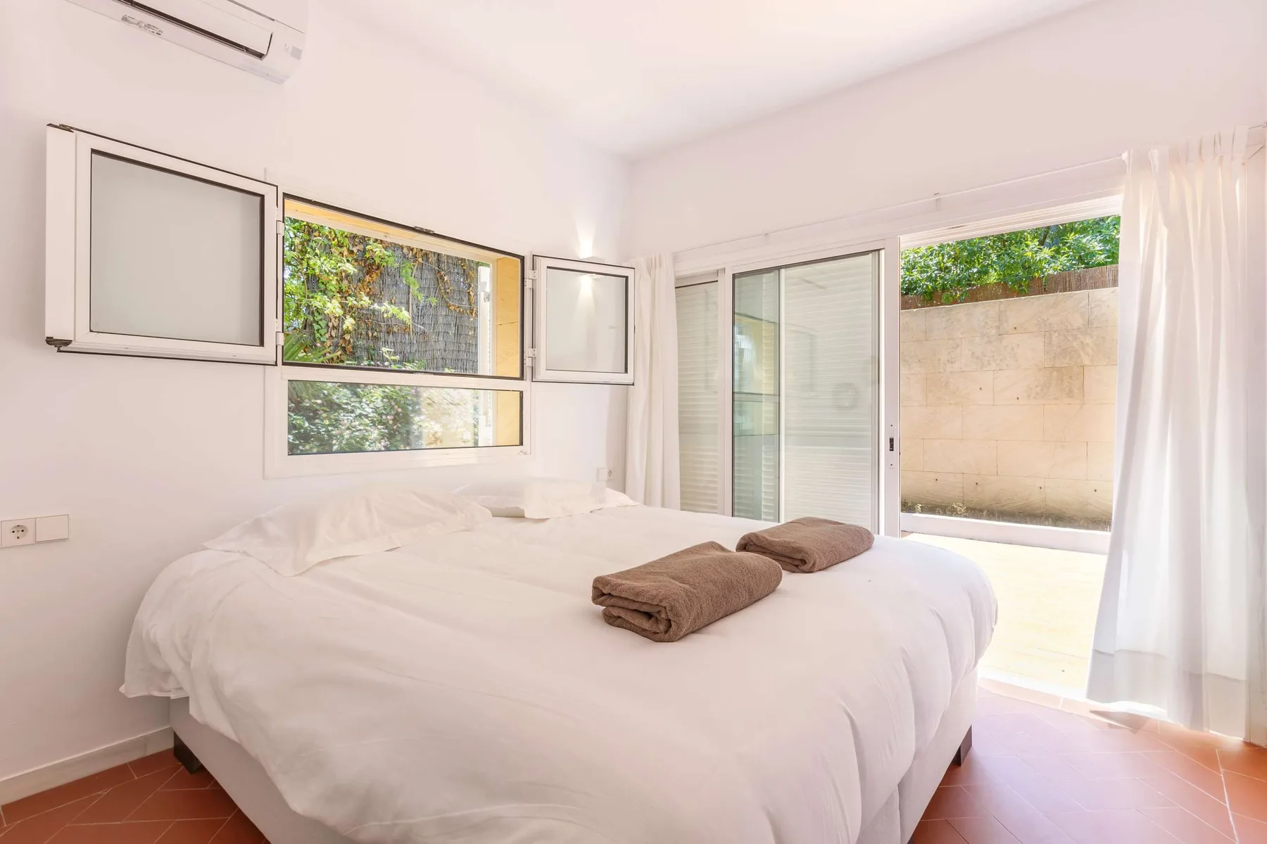 A bright bedroom with a large bed and sliding glass doors opening to a patio.