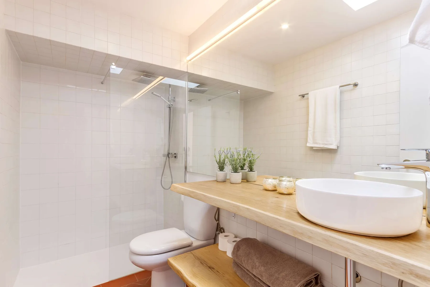 A bright tiled bathroom with a glass shower and a wide vanity.