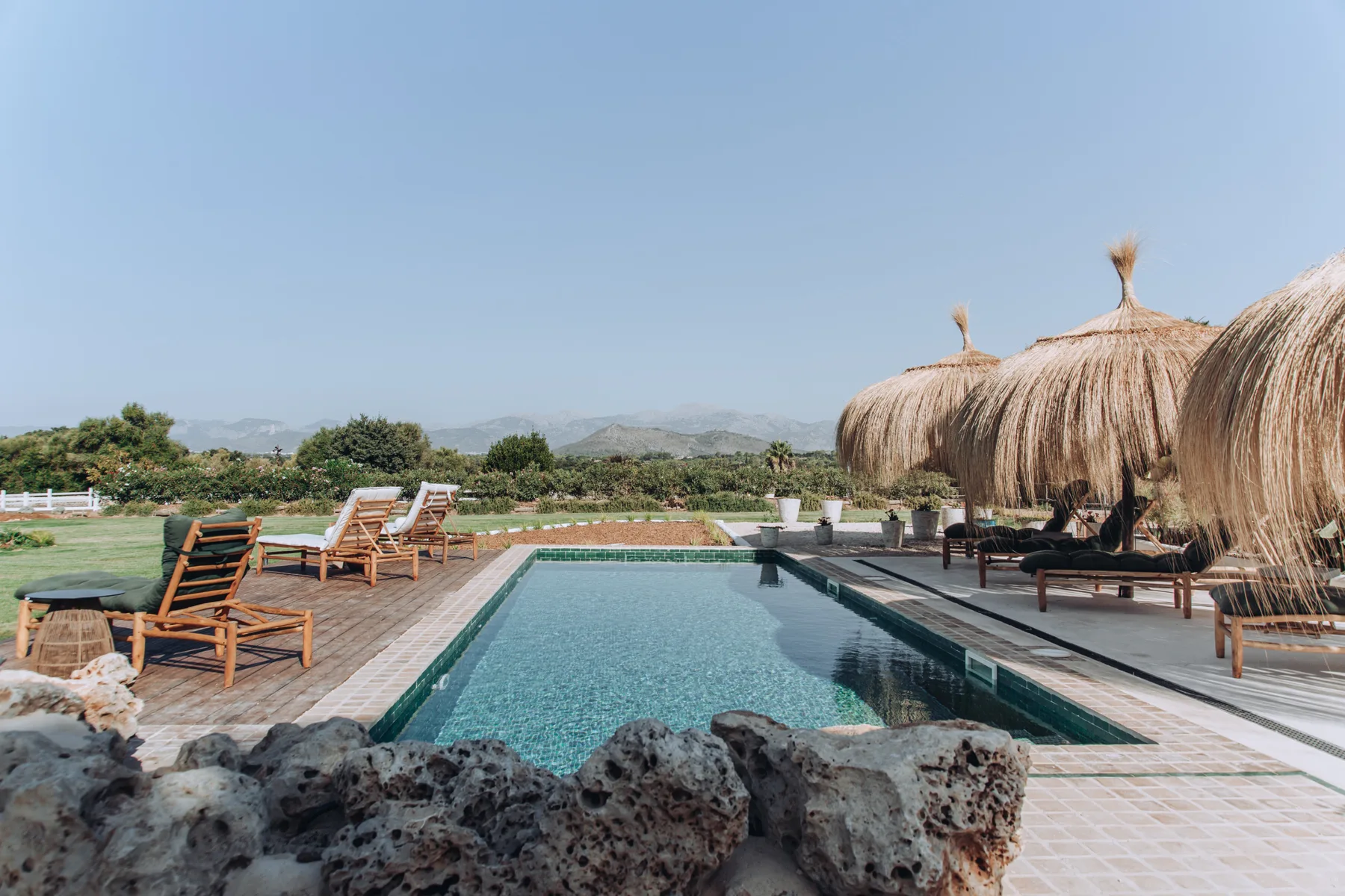 An outdoor swimming pool is surrounded by lounge seating and thatched umbrellas.