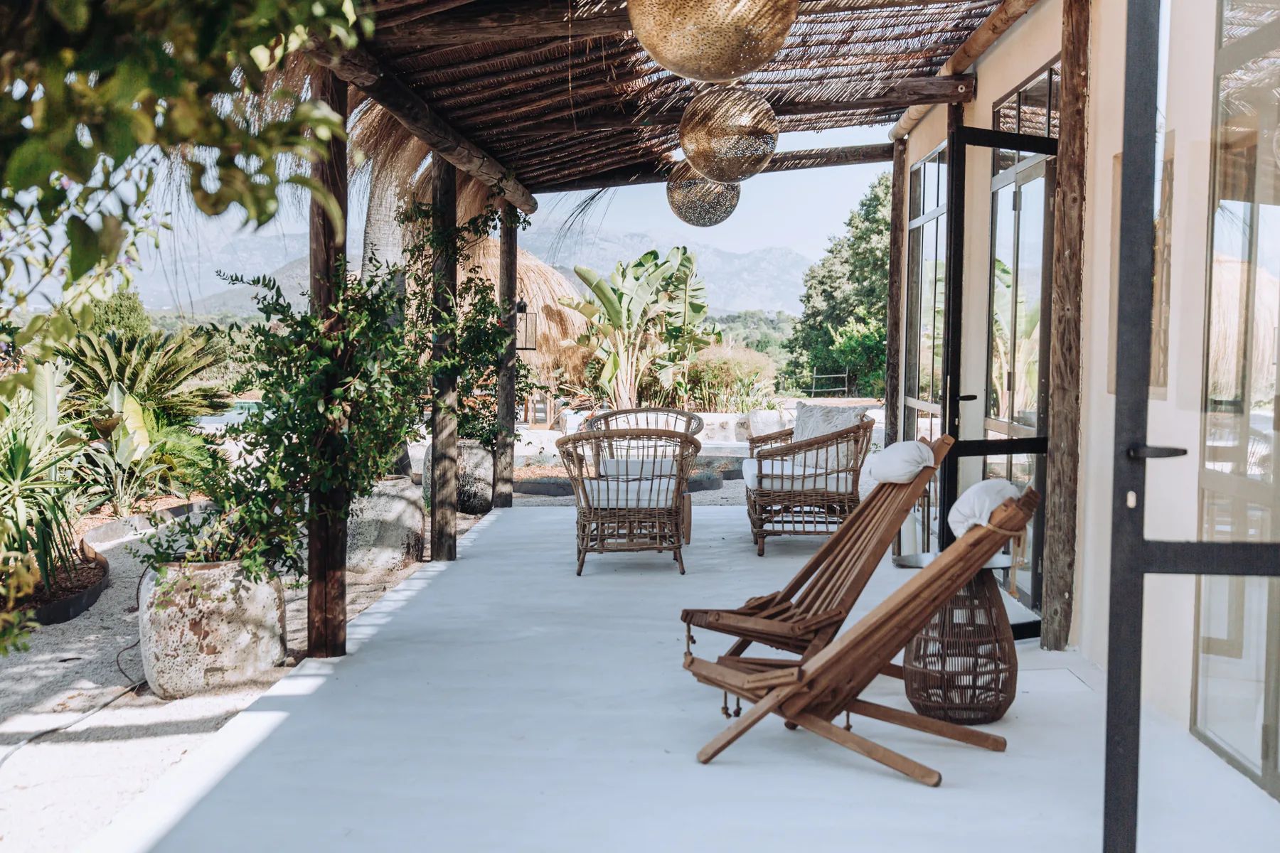 A covered outdoor patio with seating overlooks a landscaped garden and distant hills.