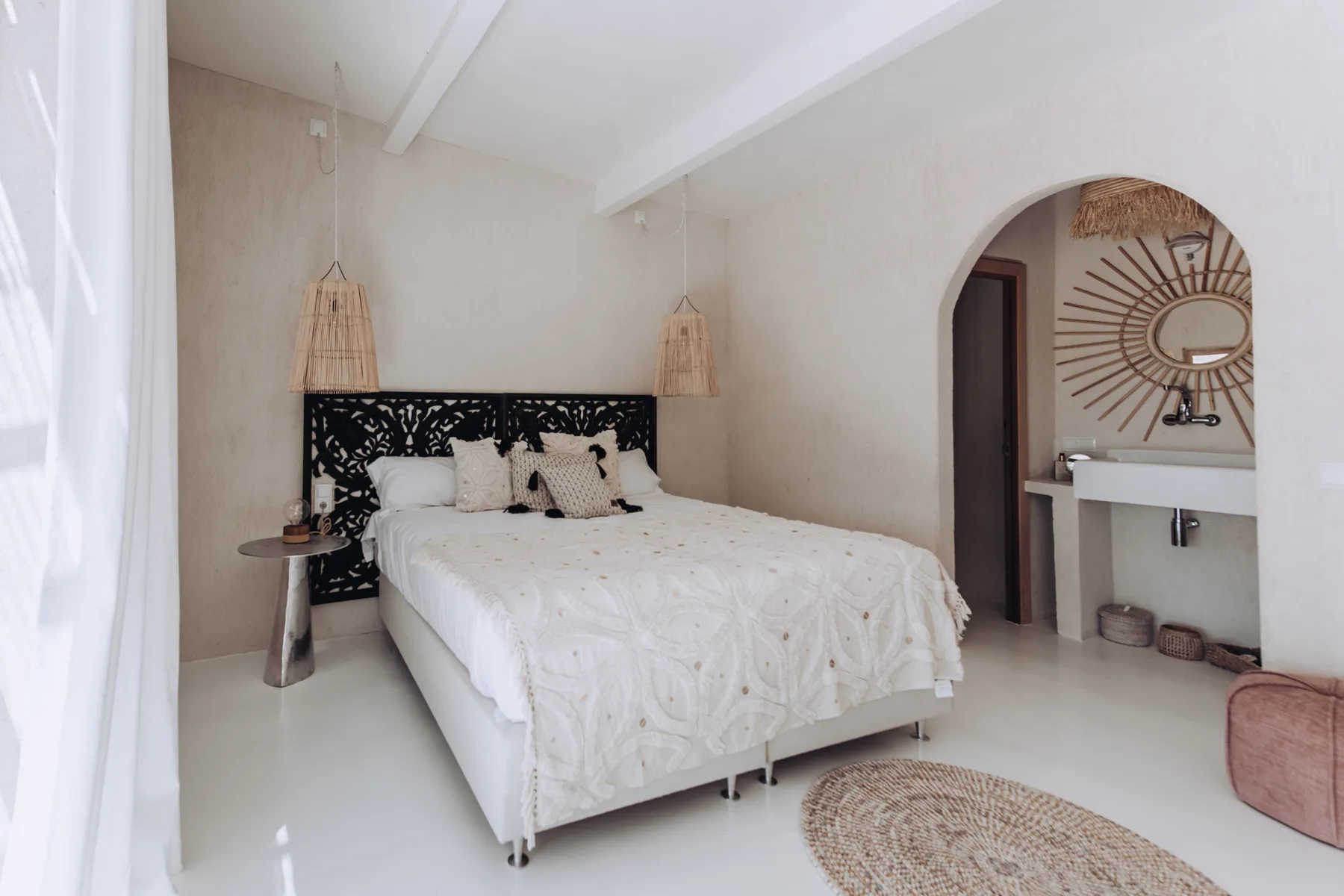 A bright bedroom with a bed and an arched opening to a washbasin.