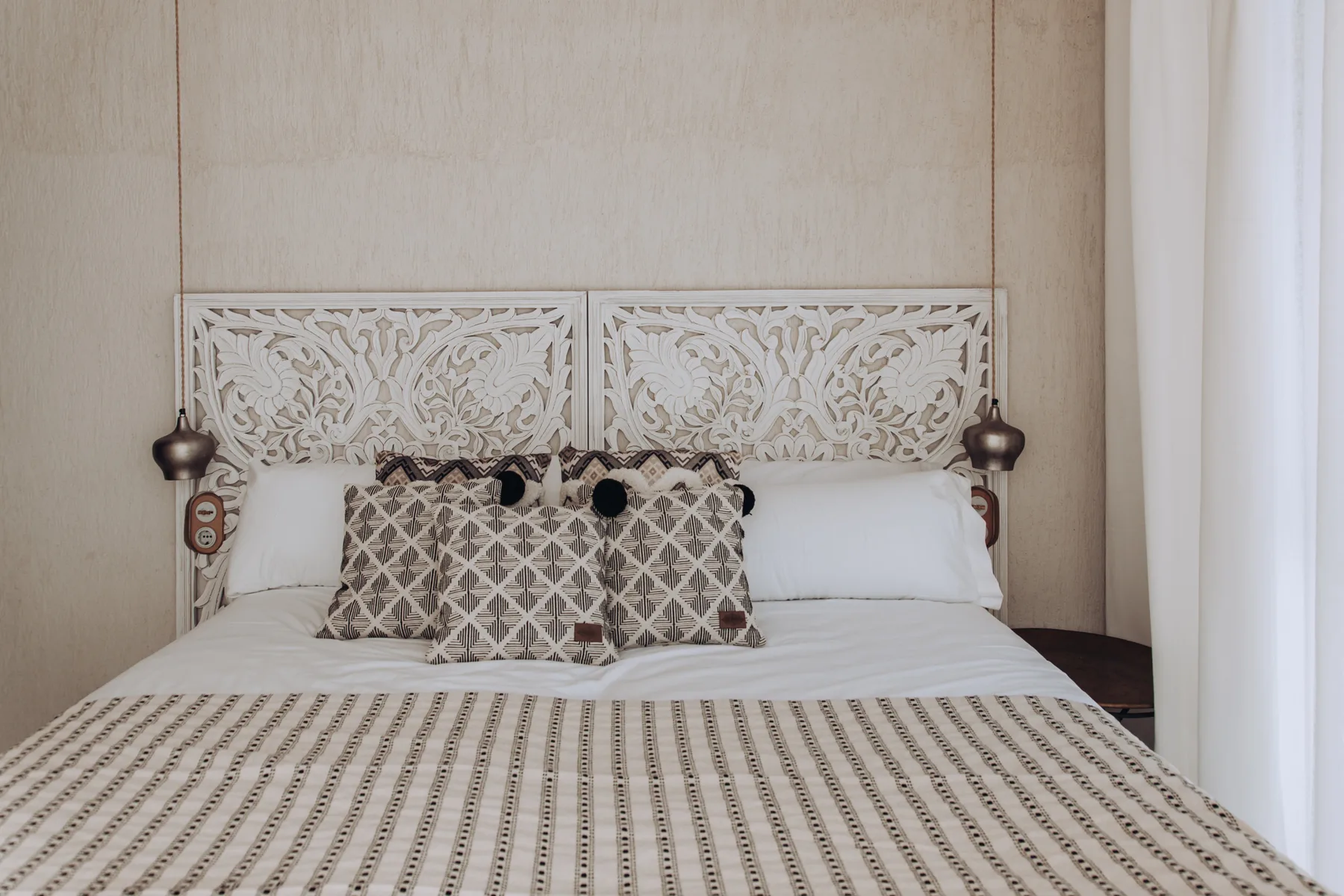 A bedroom with patterned cushions arranged across a neatly made bed.