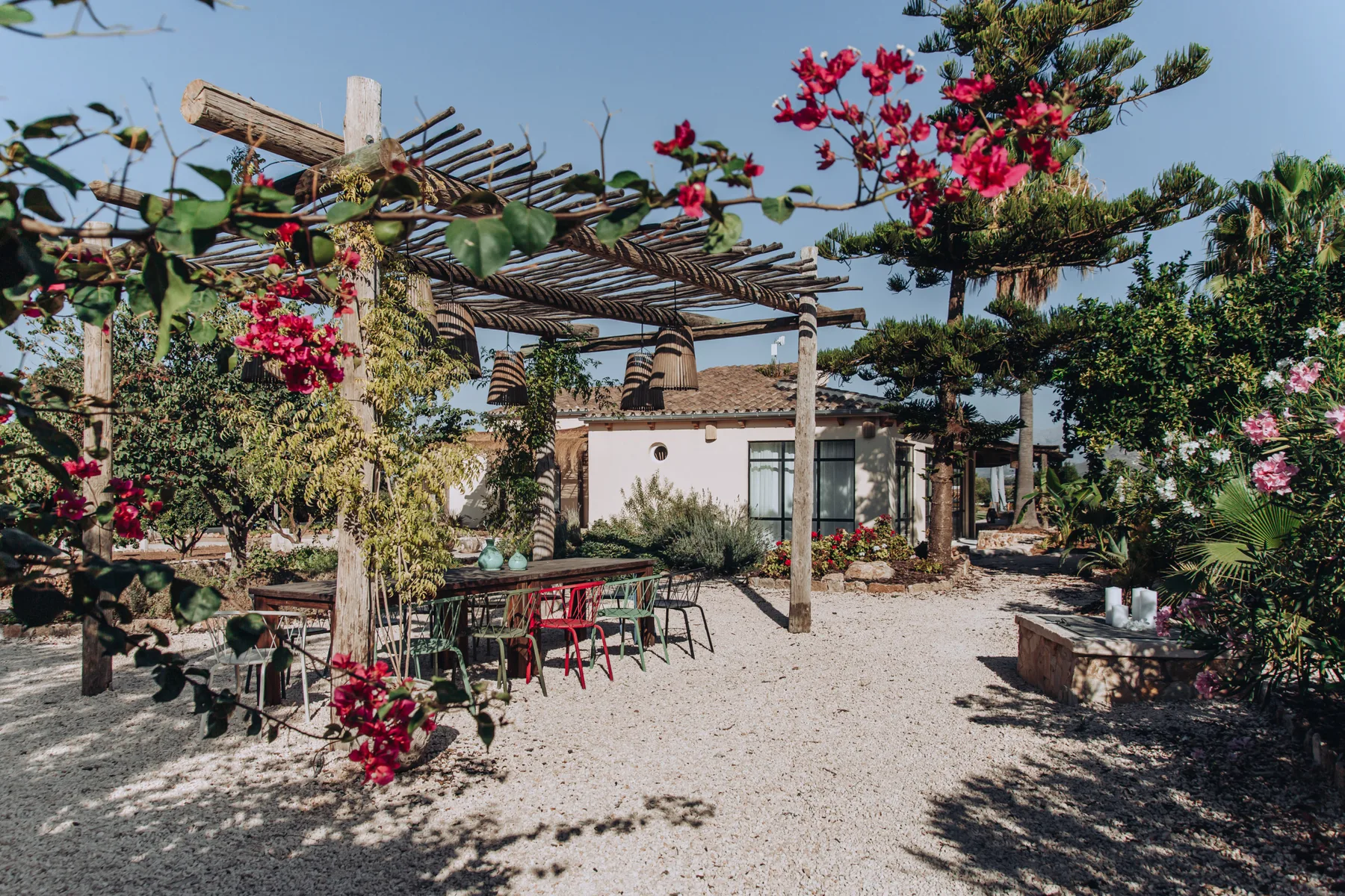 A garden patio with outdoor seating sits beside a house beneath a wooden pergola.