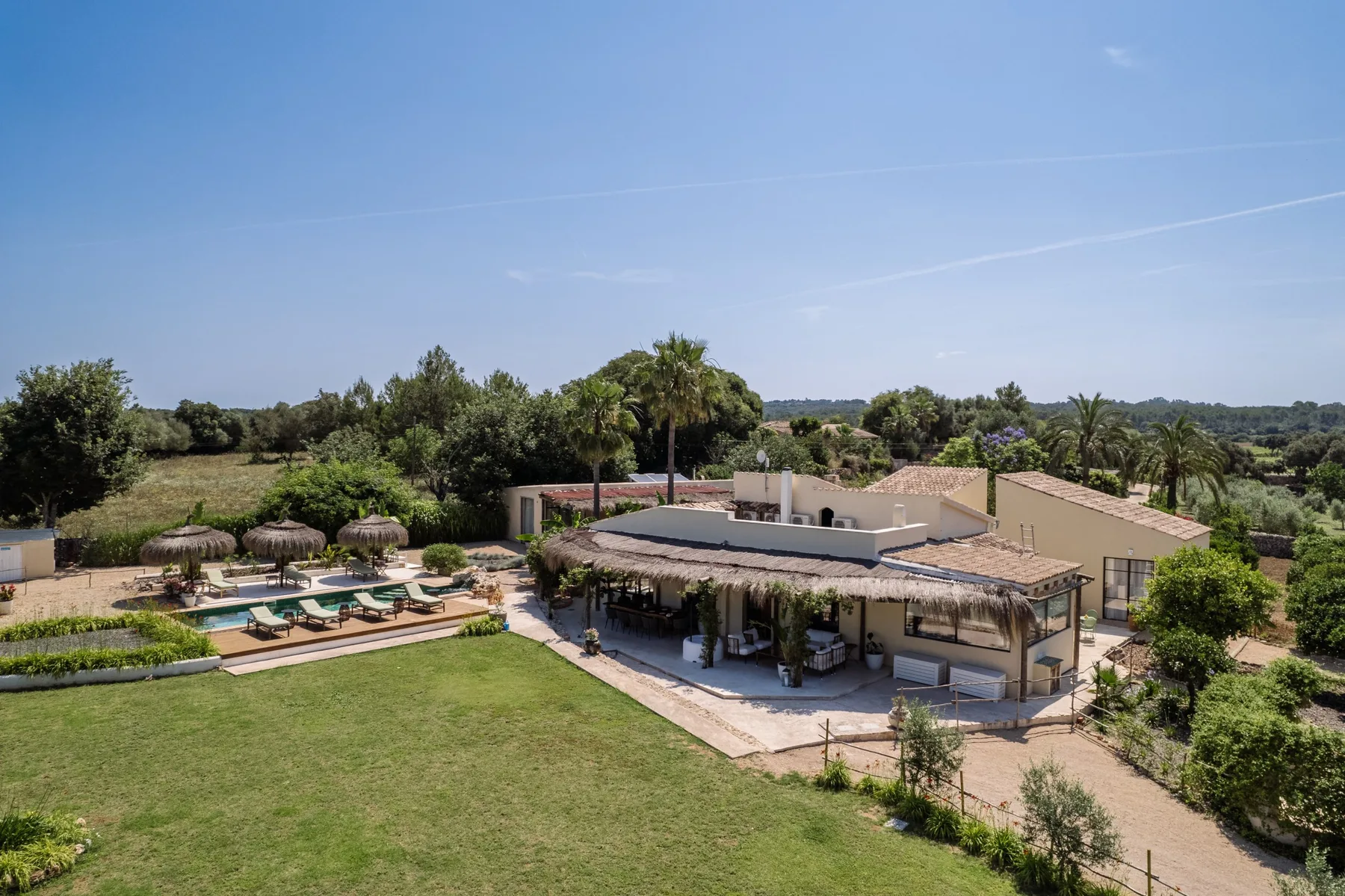 A low building overlooks a lawn, with a pool and lounge seating nearby.