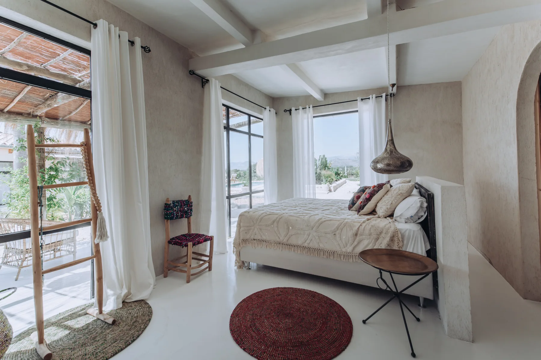 A bright bedroom with a bed, white curtains, and large windows.