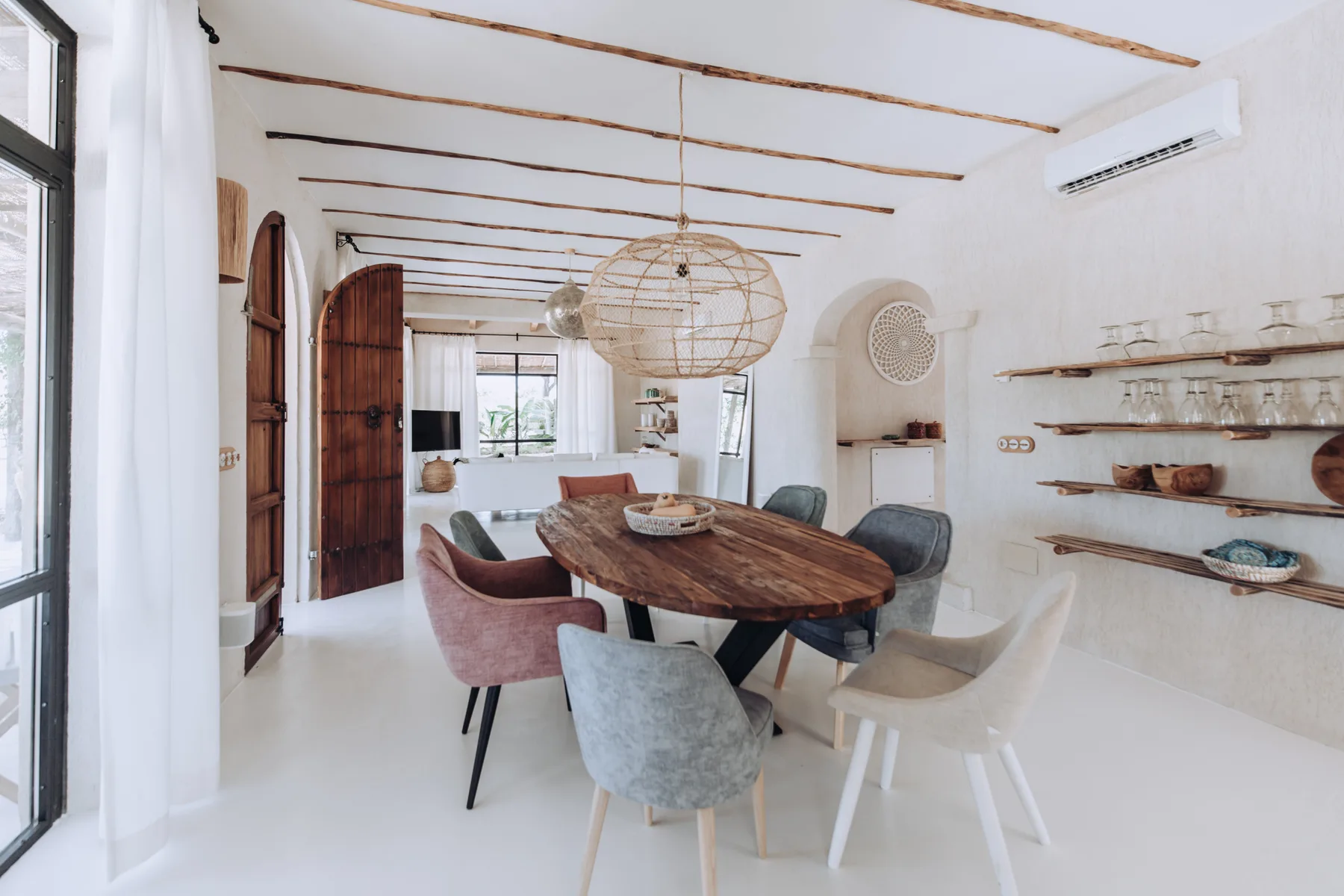A dining area with a wooden table and several seats beneath a woven pendant light.
